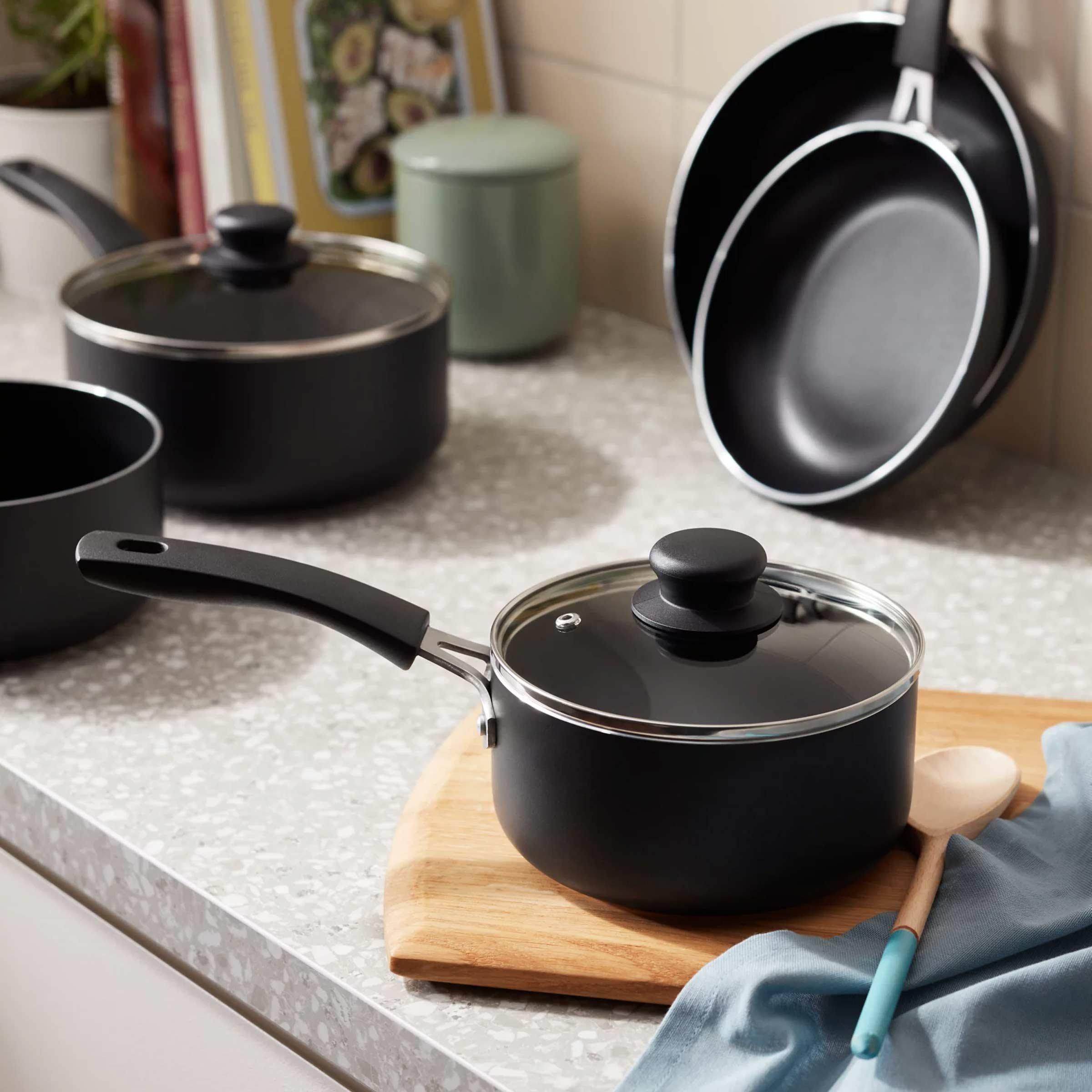 Pots, pans & kitchen spoon laid out on kitchen worktop