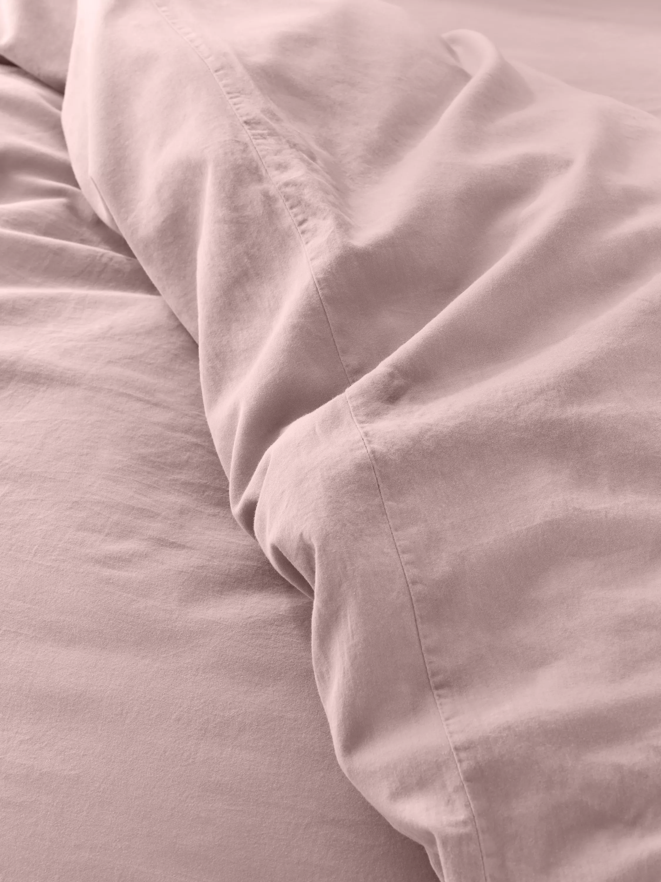 Close-up of soft blush pink cotton bedding with pillowcase seam detail, smooth sheets and cosy texture