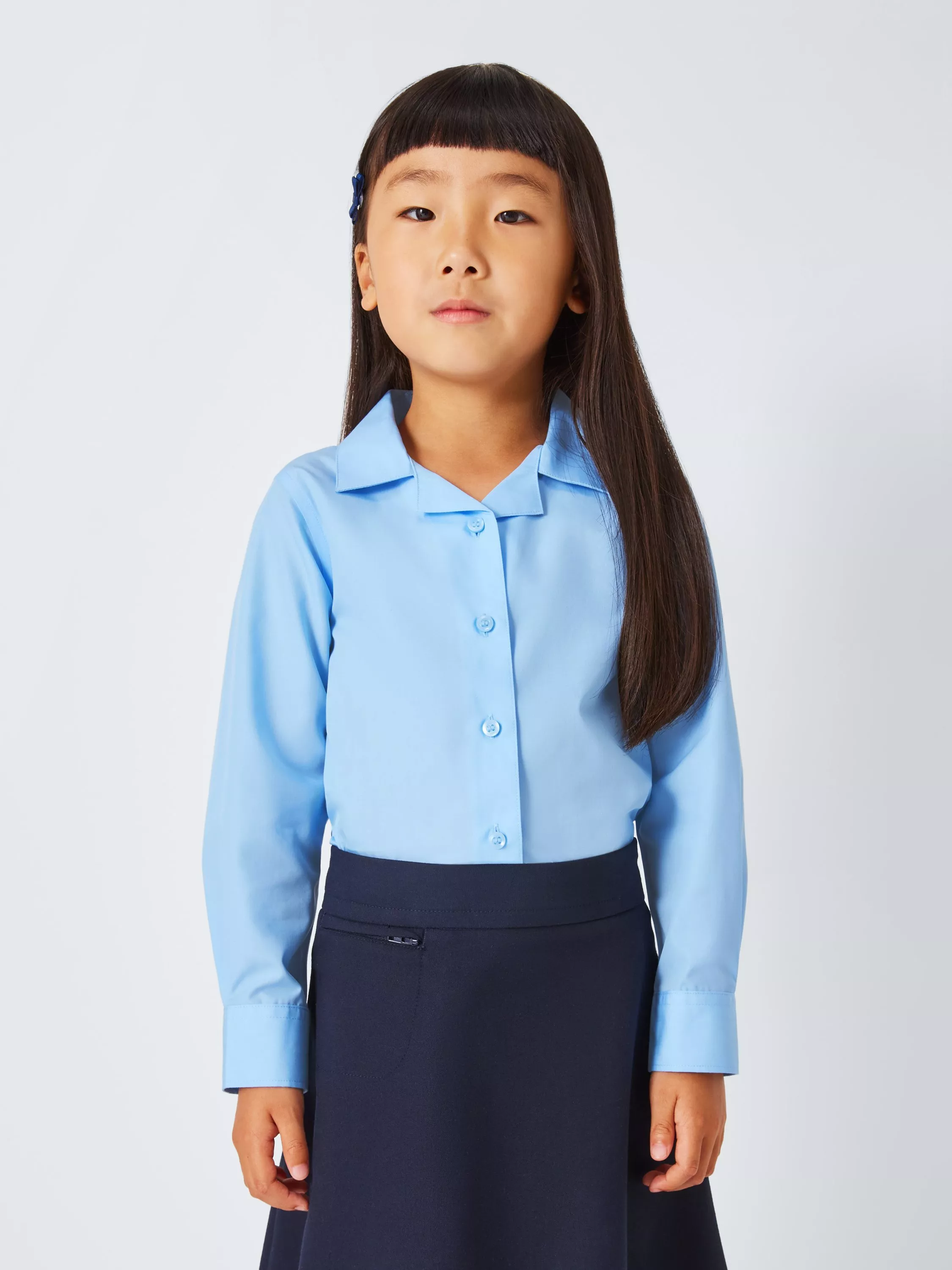 Primary school pupil wearing a light blue button-up blouse and navy skirt, studio portrait on white background
