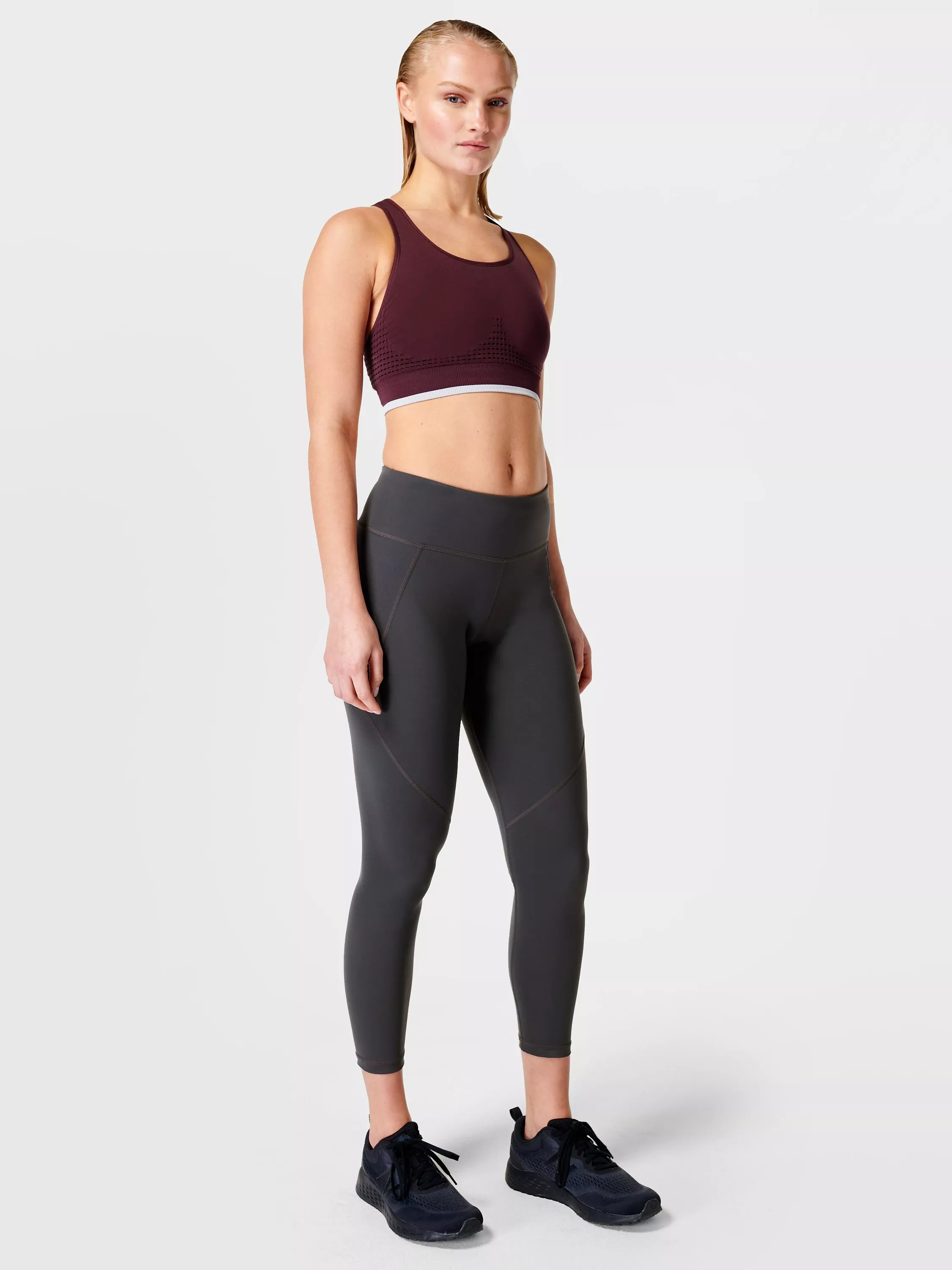Woman modelling burgundy sports bra and high-waisted grey leggings, full-length activewear outfit on white background