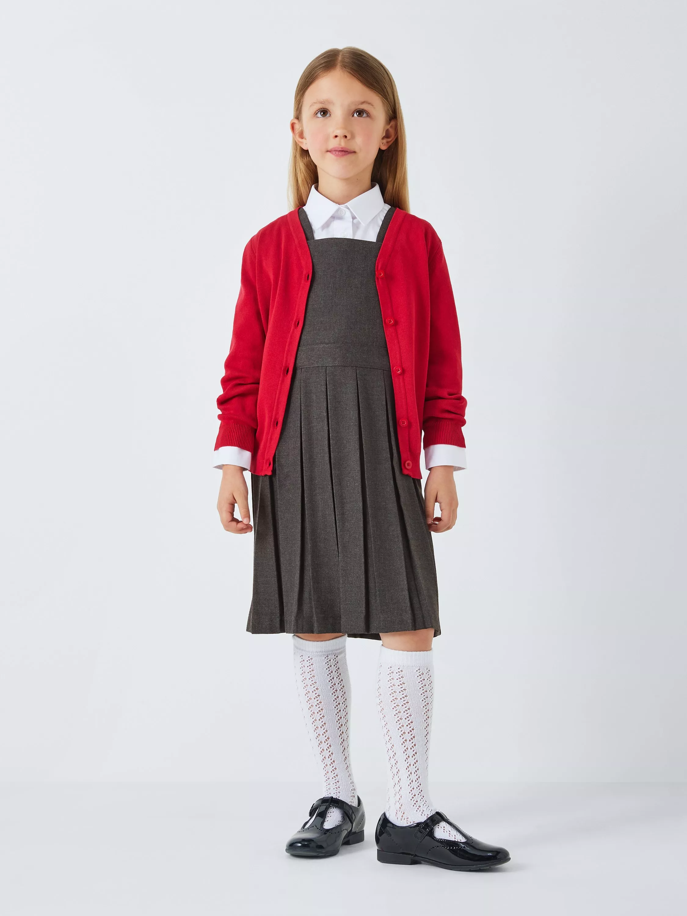 Primary school girl in grey pinafore and red cardigan, white shirt, knee socks and black shoes on studio background