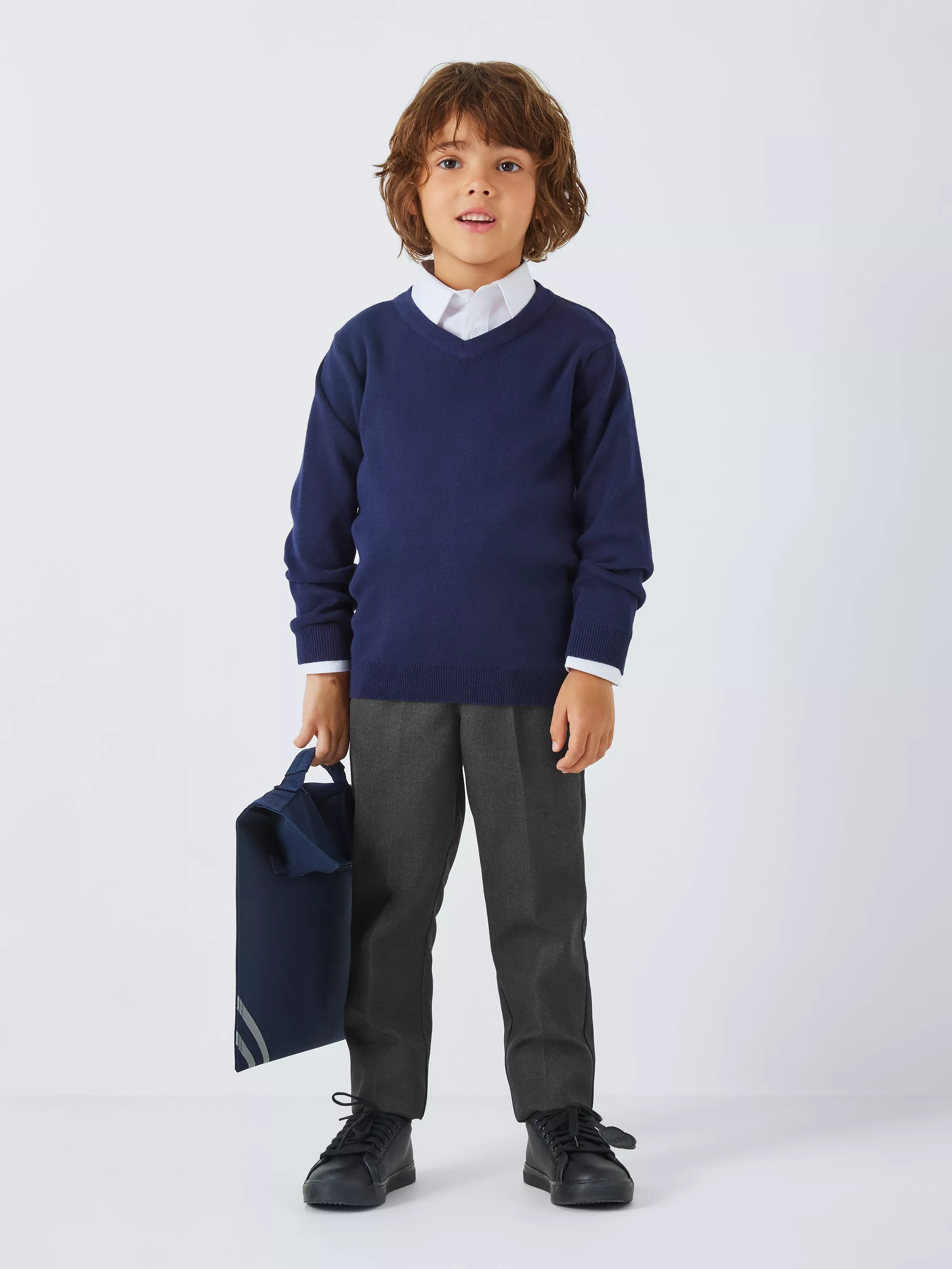 Schoolboy in navy V-neck jumper, white shirt and grey trousers, holding a navy PE bag on grey backdrop