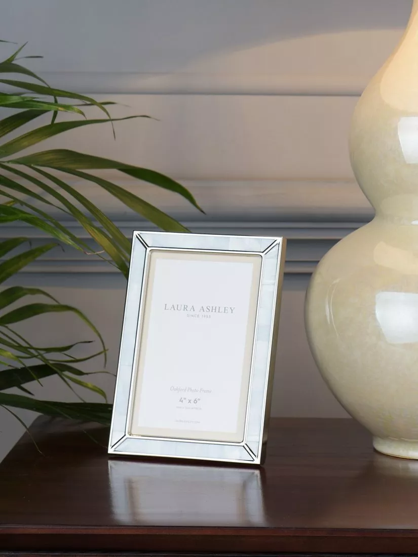 Silver mirrored photo frame on wooden sideboard with leafy plant and cream ceramic lamp, stylish home décor display