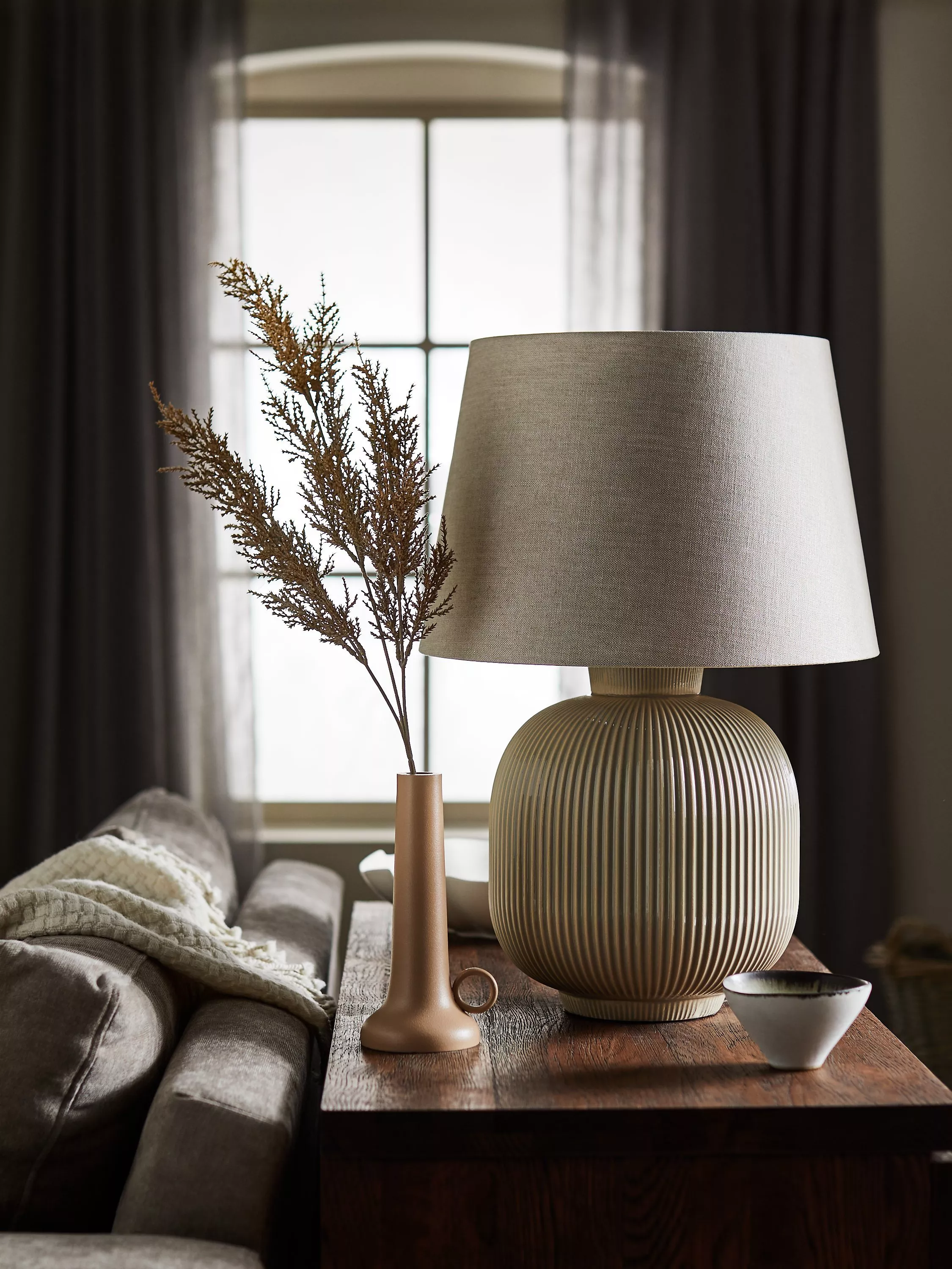 Elegant living room with a ribbed table lamp and vase on a wooden side table. Soft, natural lighting.