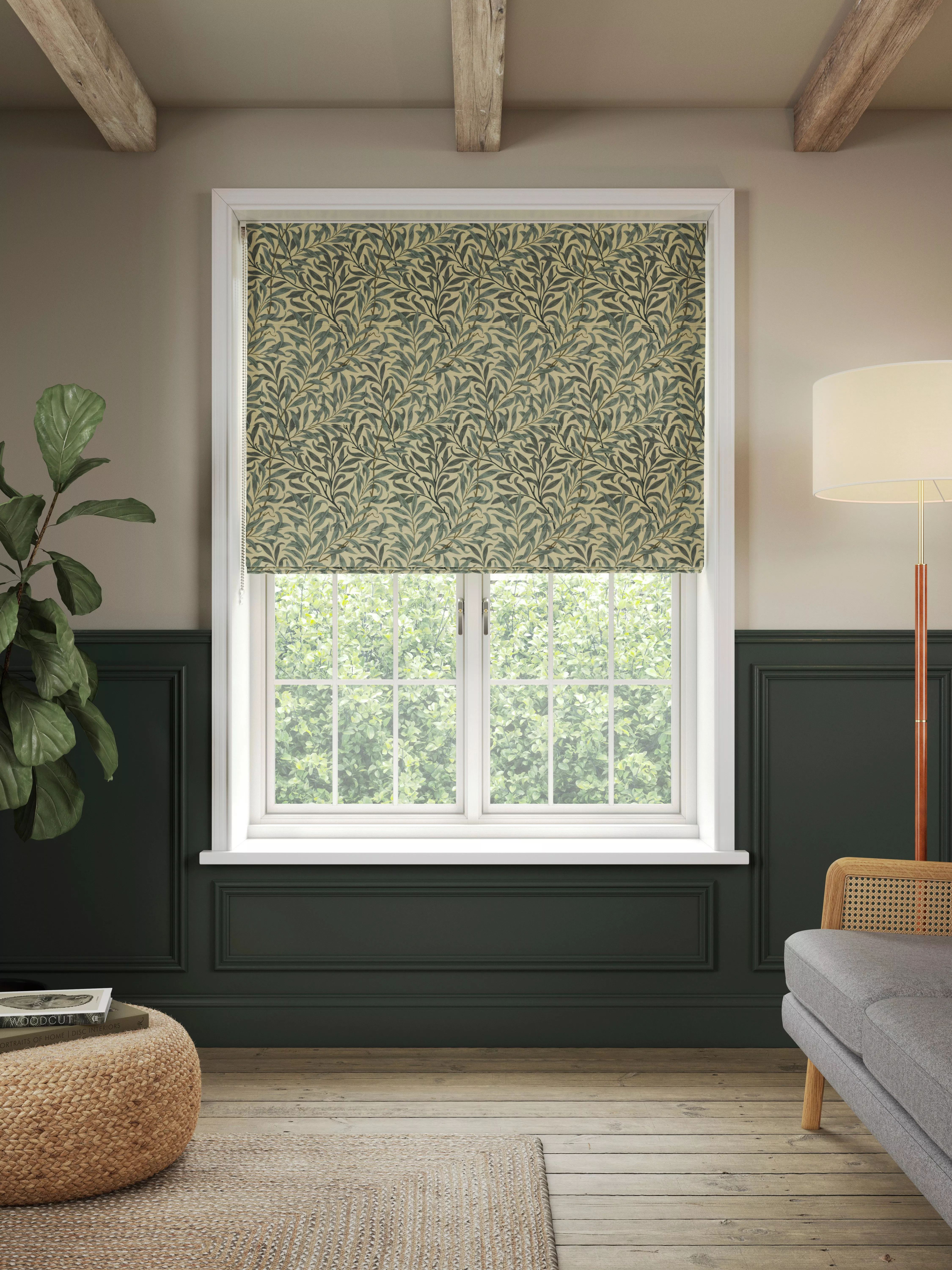 Green botanical patterned Roman blind on white sash window in modern living room with dark panelling and beams