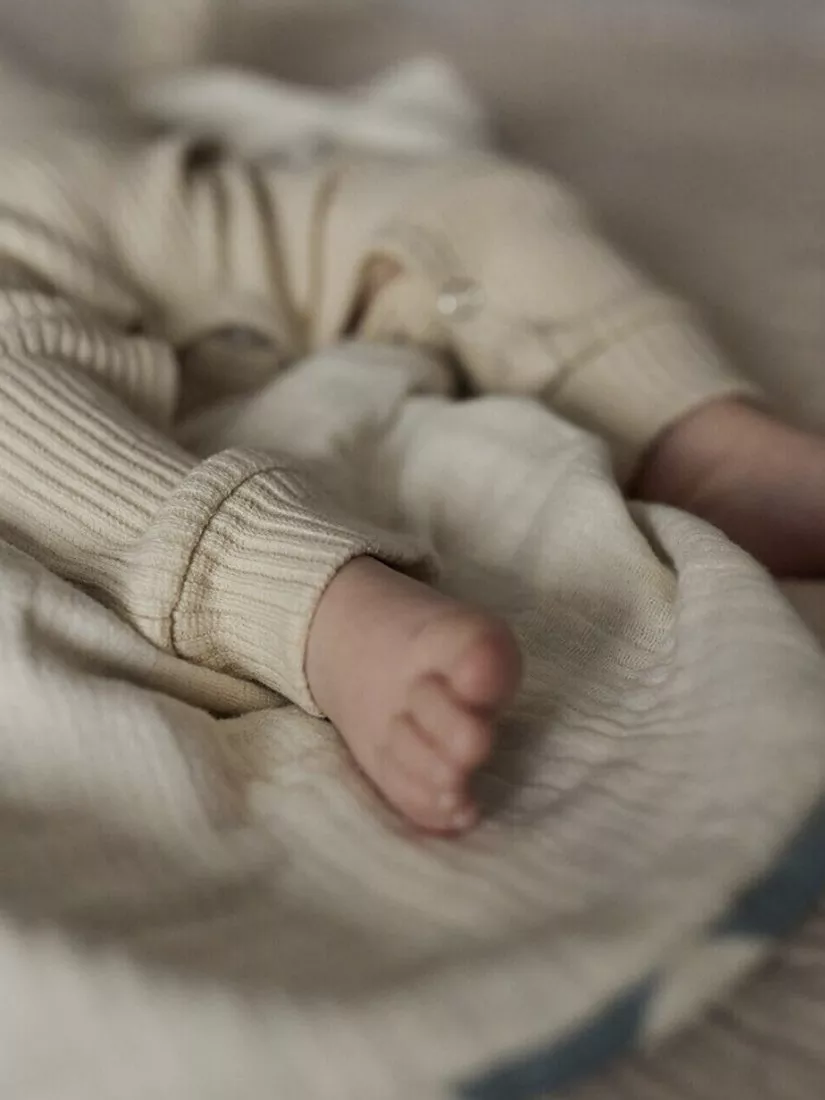 Close-up of newborn baby feet in beige knitted romper on soft blanket, cosy nursery lifestyle photography