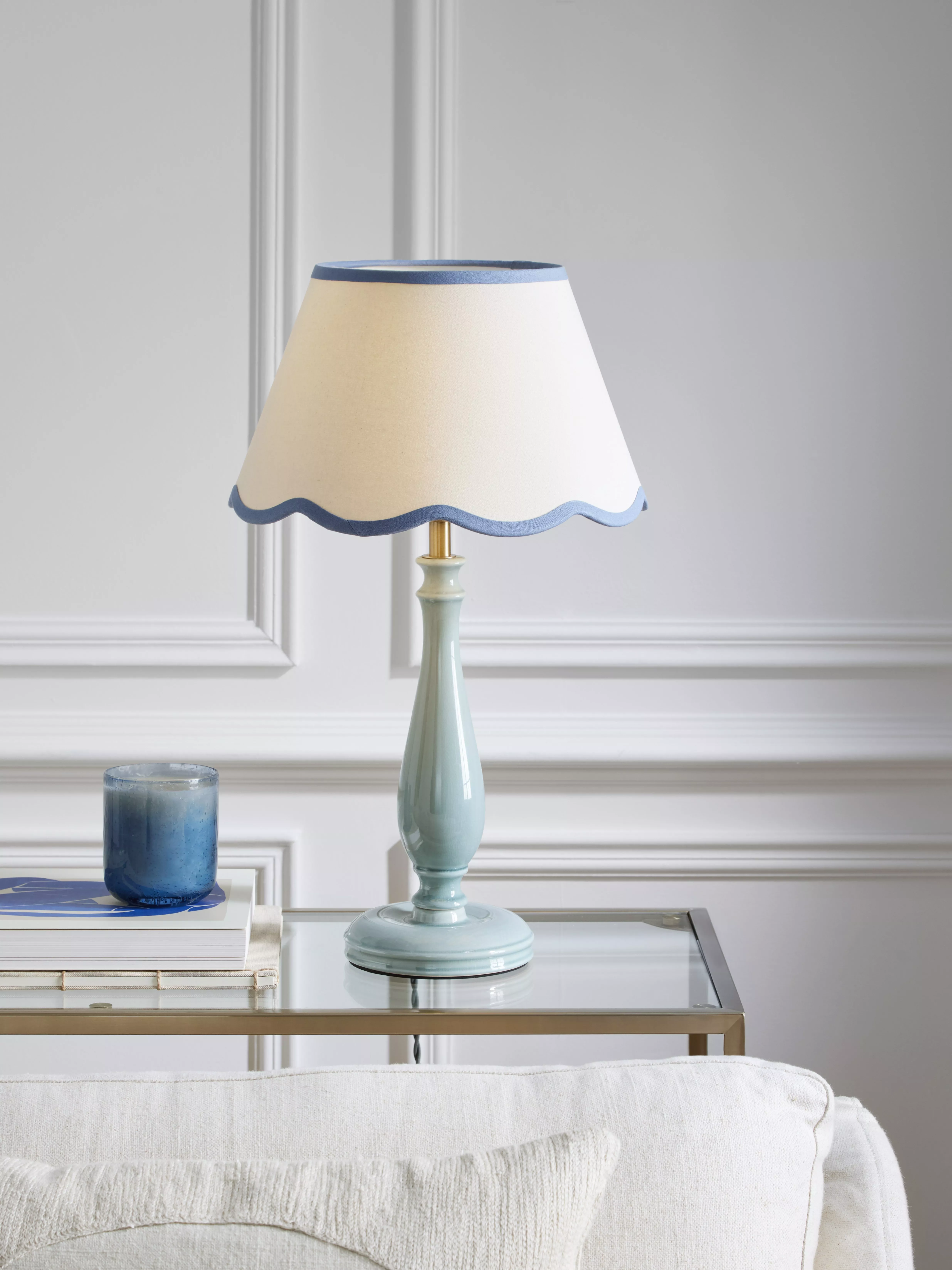 Blue ceramic table lamp with scalloped white shade on glass side table, styled living room interior décor