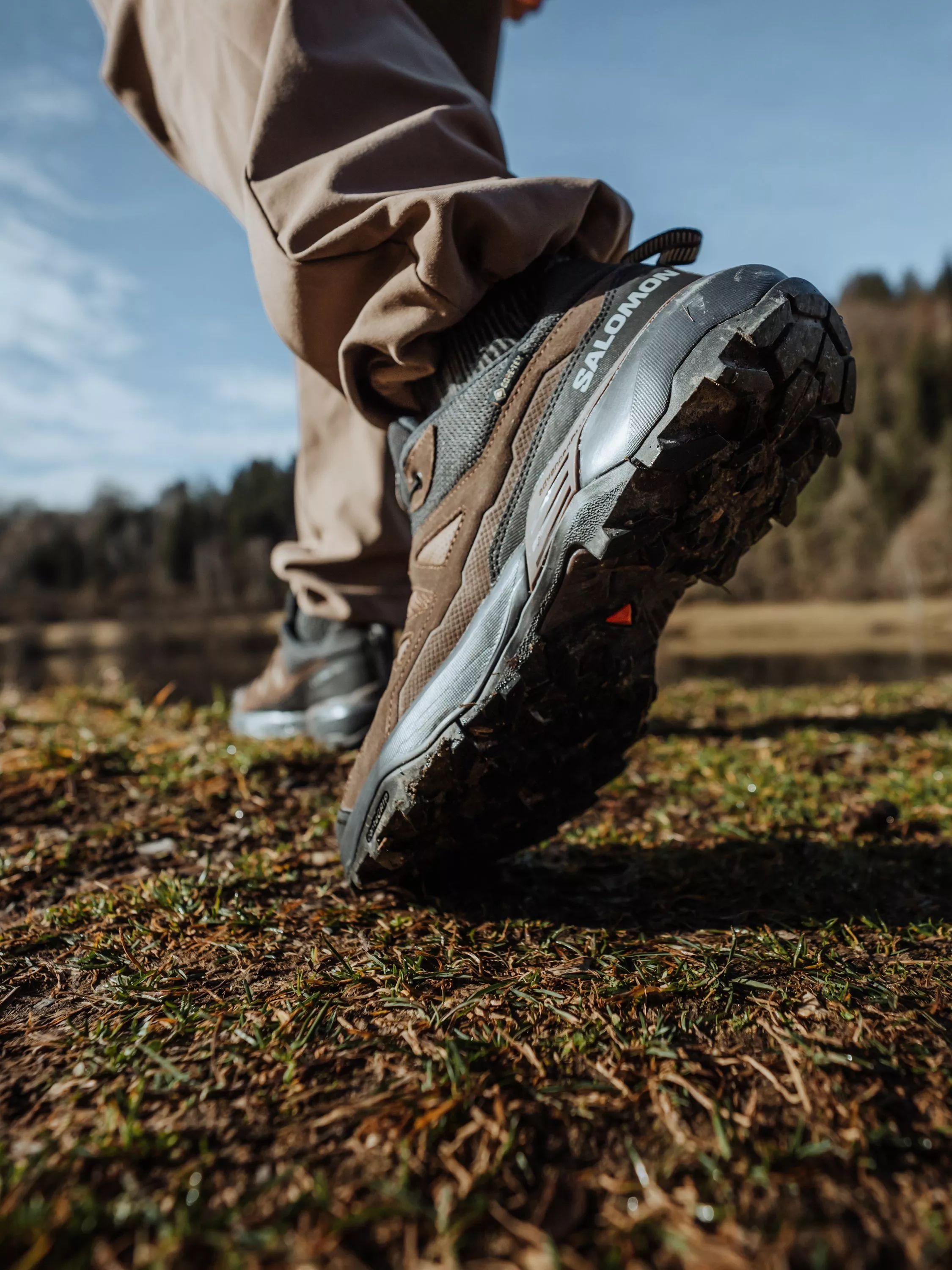 Close-up of Salomon hiking boot stepping on grassy trail outdoors, rugged sole grip in countryside light
