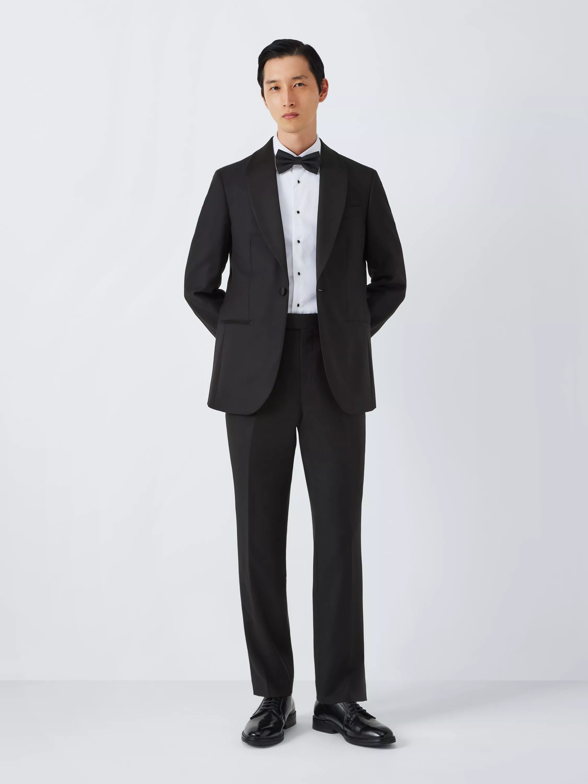 Male model wearing a black tuxedo with satin lapels, white dress shirt and bow tie on a white background