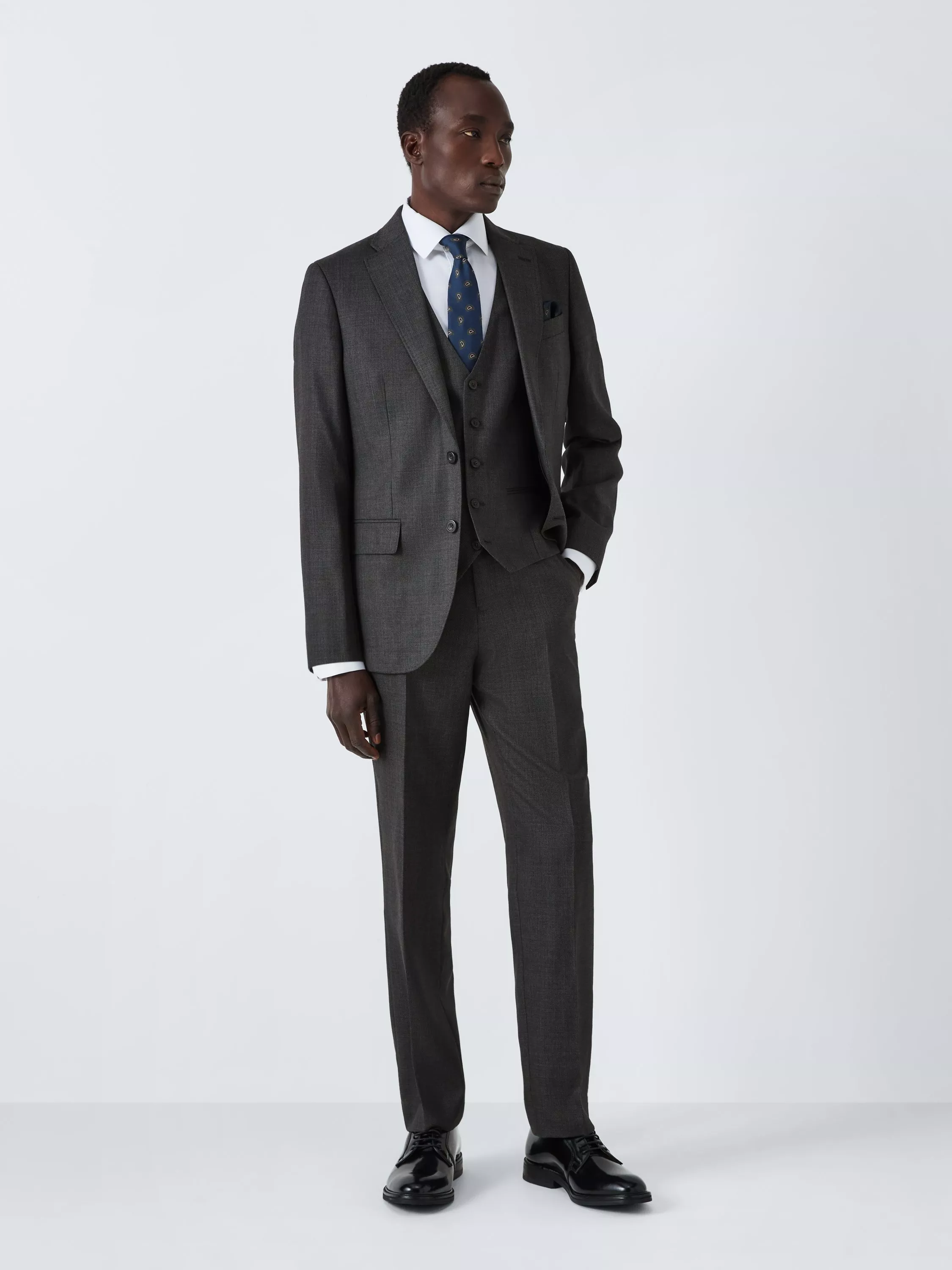 Male model wearing a charcoal grey two-piece suit with white shirt and blue patterned tie on a studio background
