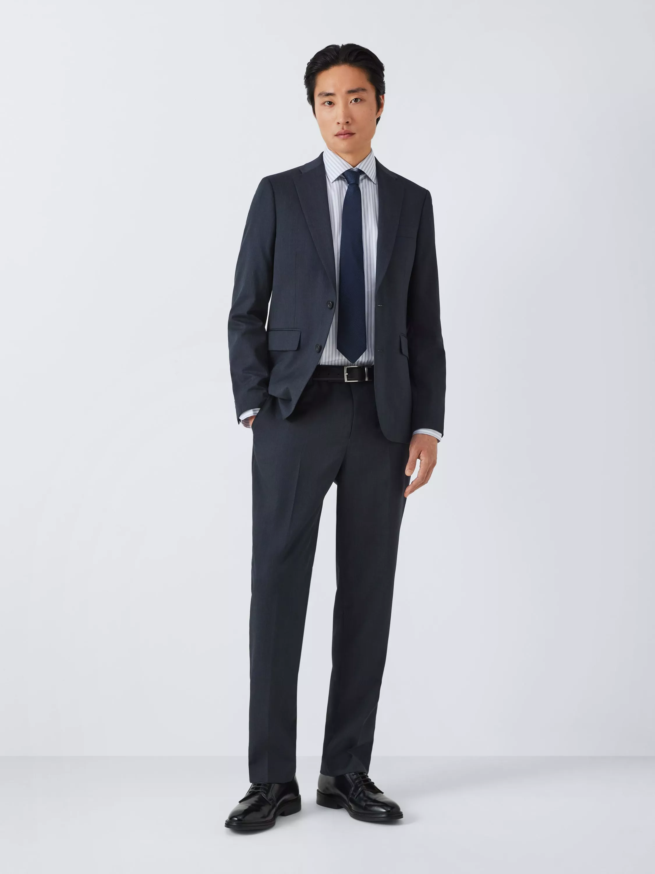 Male model wearing a navy business suit with light blue shirt and striped tie, studio portrait on grey background