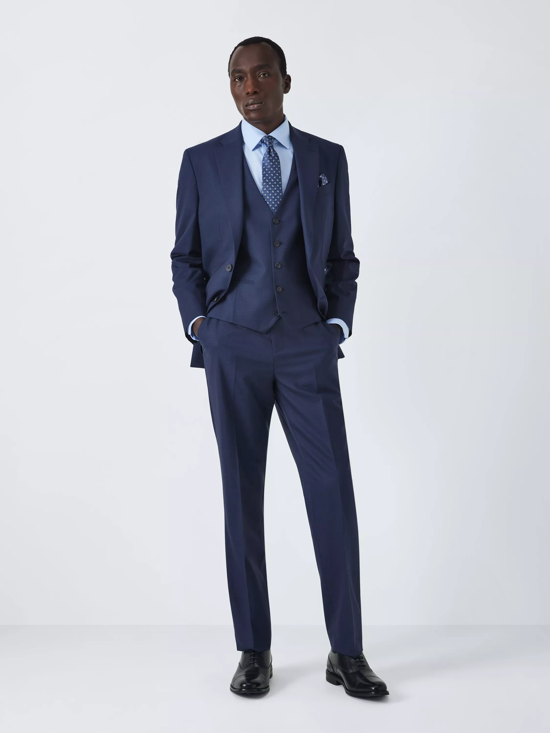 Male model wearing an olive green three-piece suit with waistcoat, white shirt and tie, studio portrait view