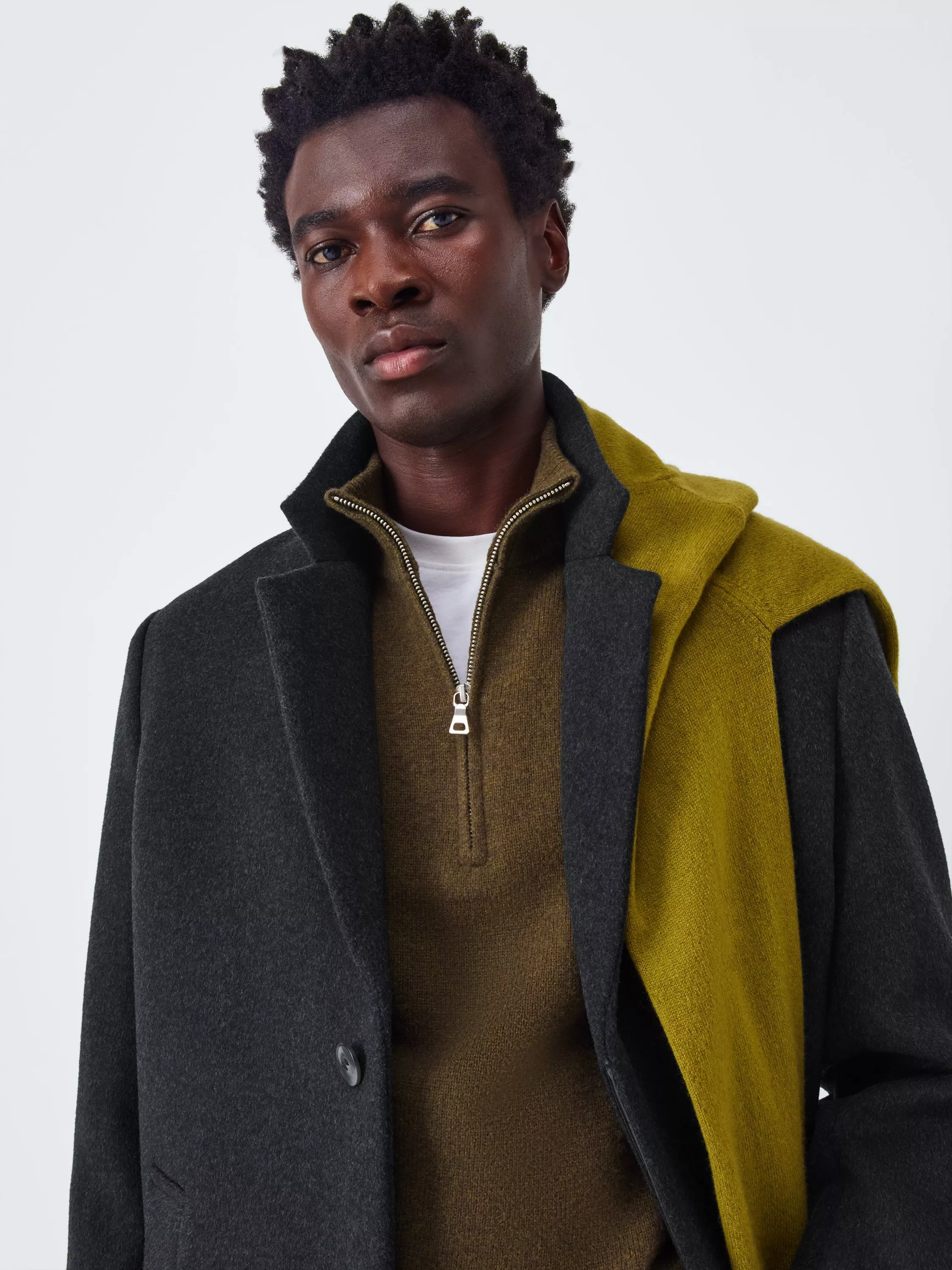 Man wearing a half zip jumper with overcoat on top, and jumper around his shoulder