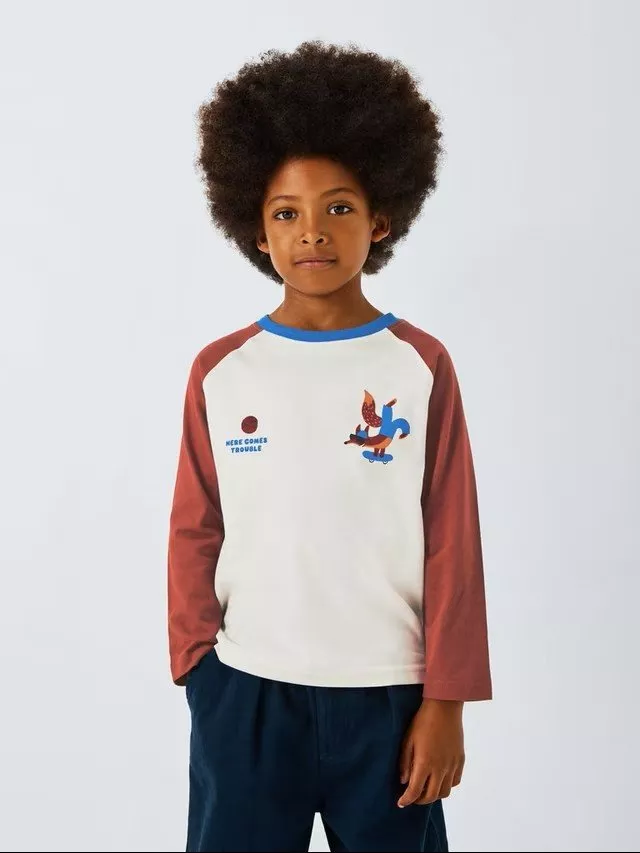 Young boy in white and rust raglan long-sleeve T-shirt with dinosaur skateboard print, studio portrait on grey backdrop