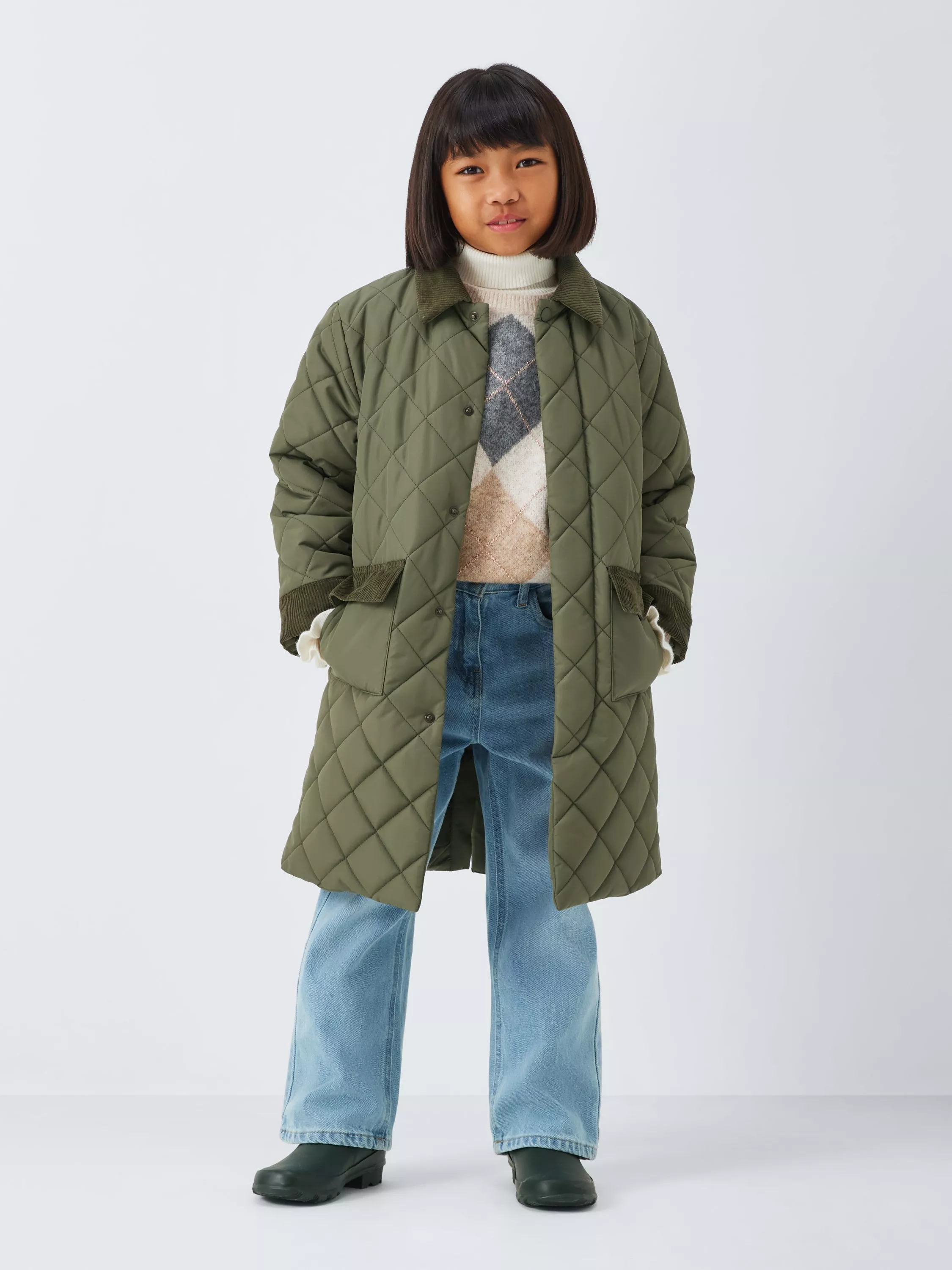 A girl with short dark hair wearing a long, olive green quilted coat with a corduroy collar and cuffs