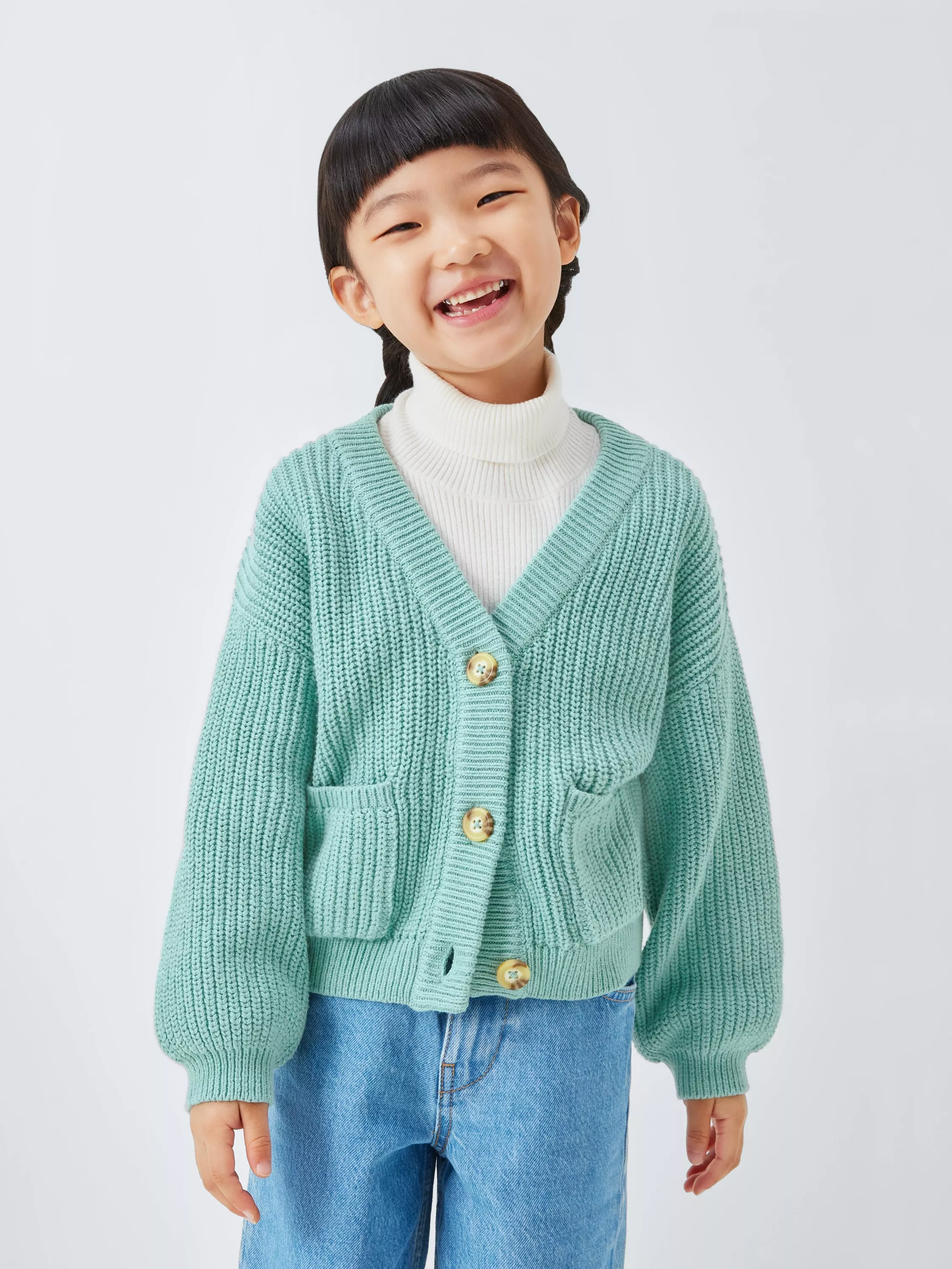 A child in a mint green knit cardigan and a white turtleneck.