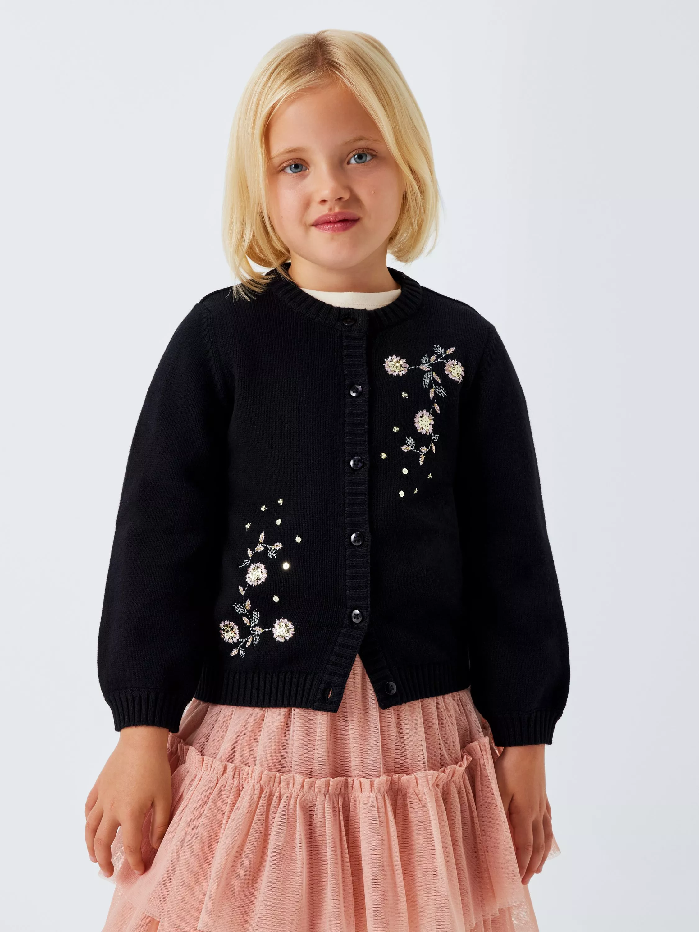 A child in a blue embroidered cardigan and pink skirt