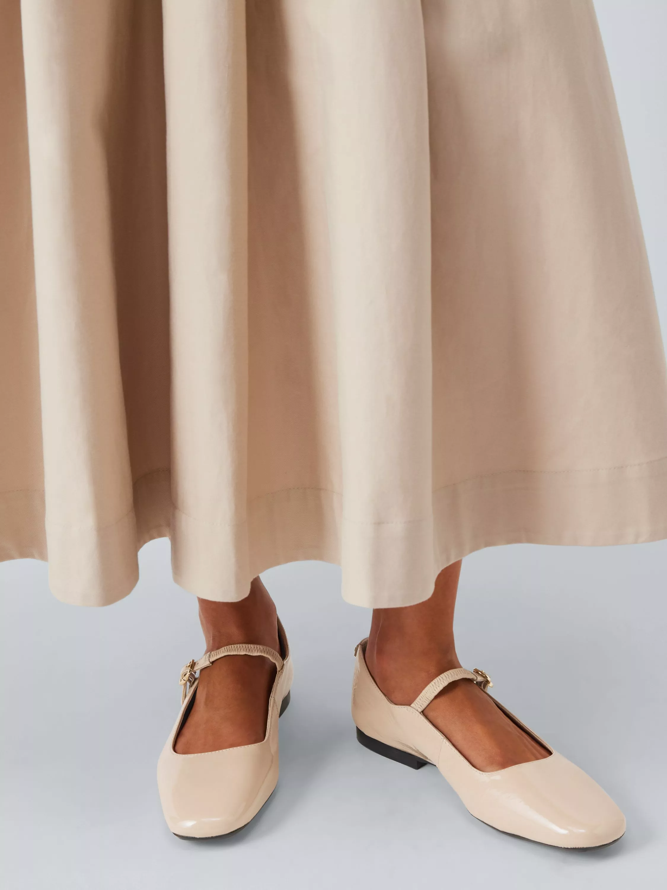 Beige patent Mary Jane flats with buckle strap, worn with a cream midi skirt hem, close-up on feet.