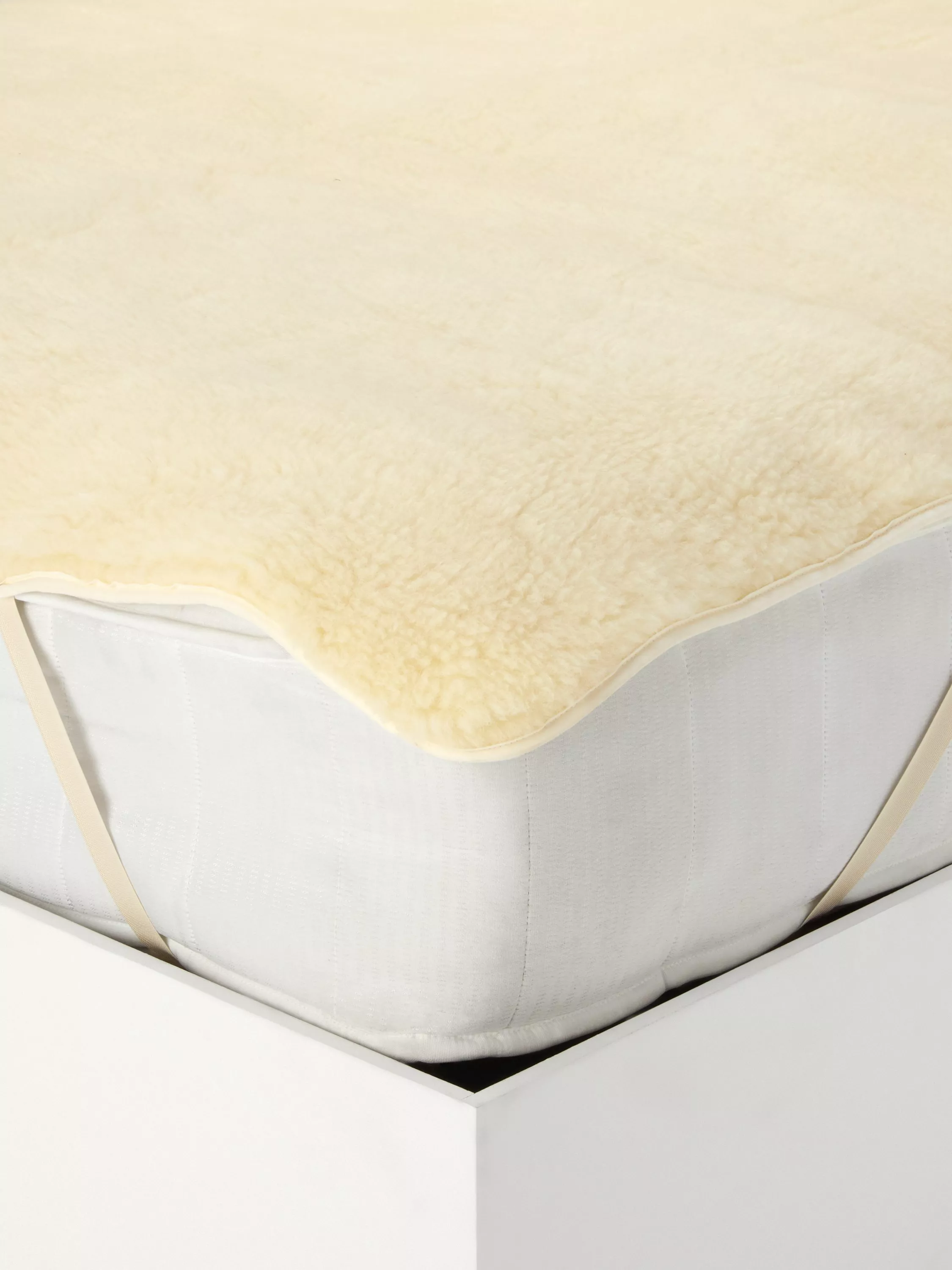 Soft wool mattress topper secured with elastic straps on a white bed frame, providing extra comfort and warmth.