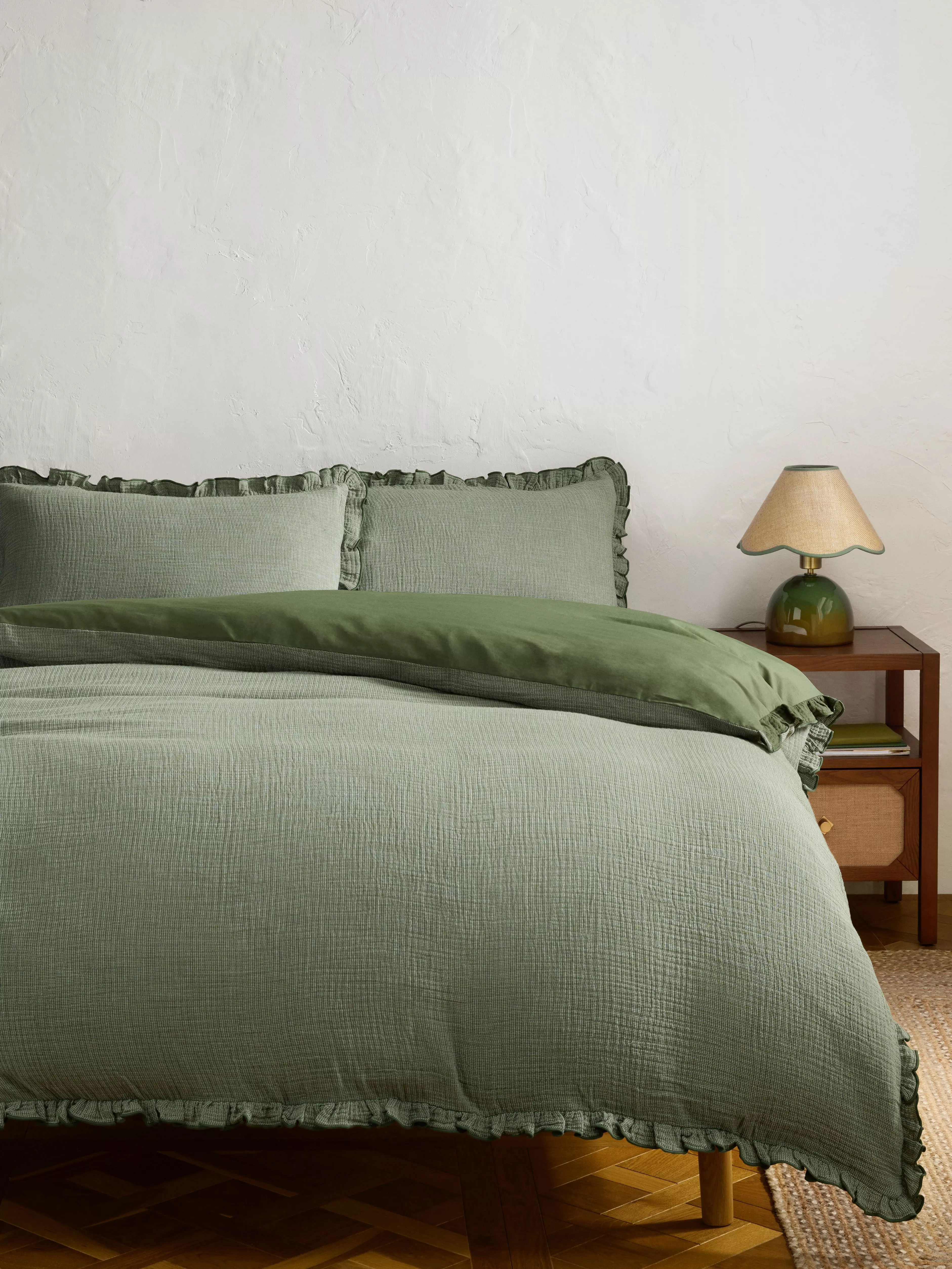 Sage green ruffled duvet cover set on bed, minimalist bedroom decor with wooden bedside table and lamp