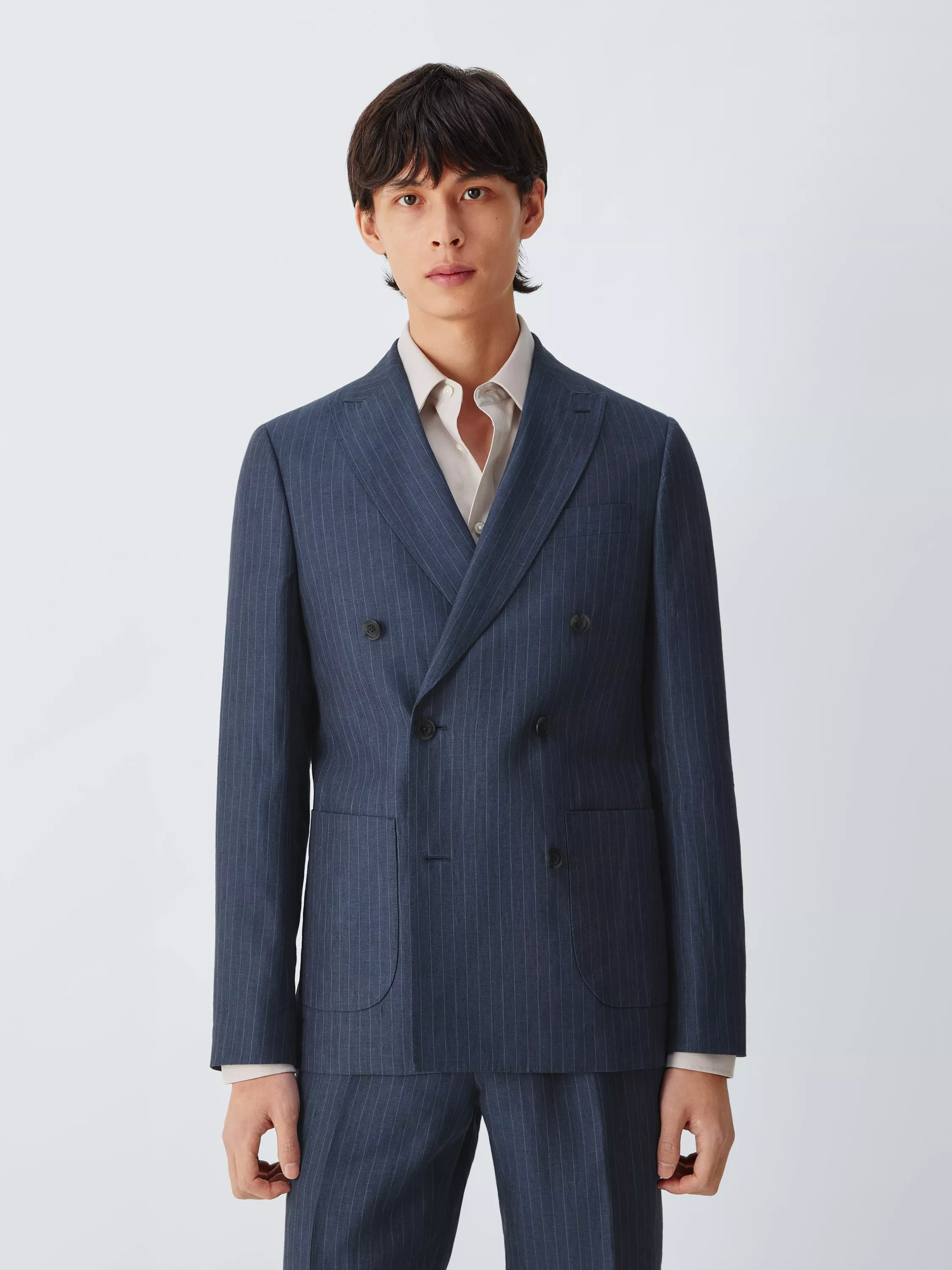 Studio portrait of male model wearing a navy pinstripe double-breasted suit and white shirt on grey background
