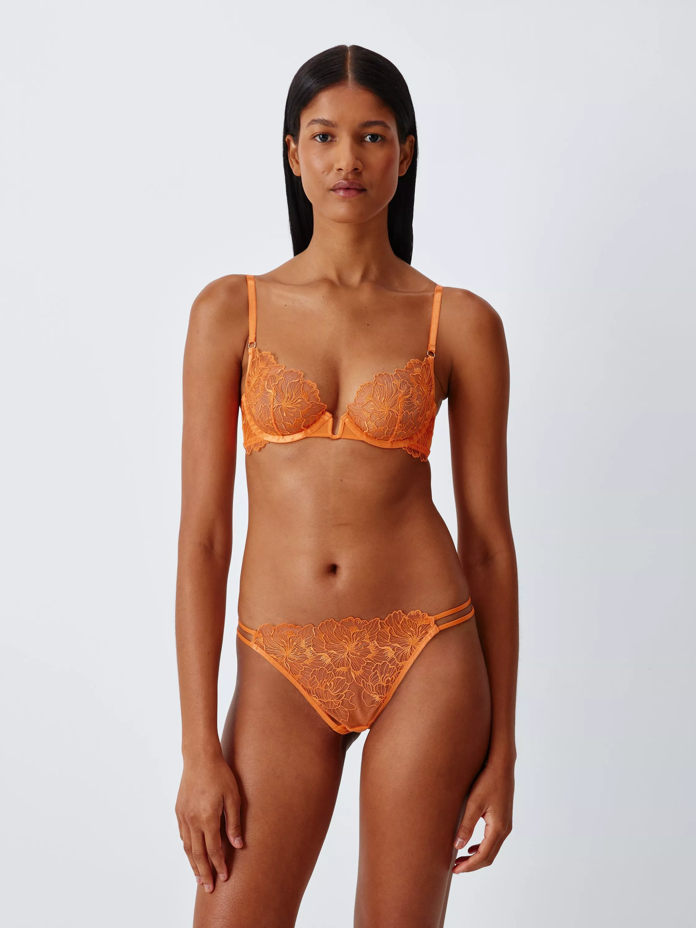 Model wearing orange floral lace lingerie set with underwired bra and matching briefs on a plain studio background