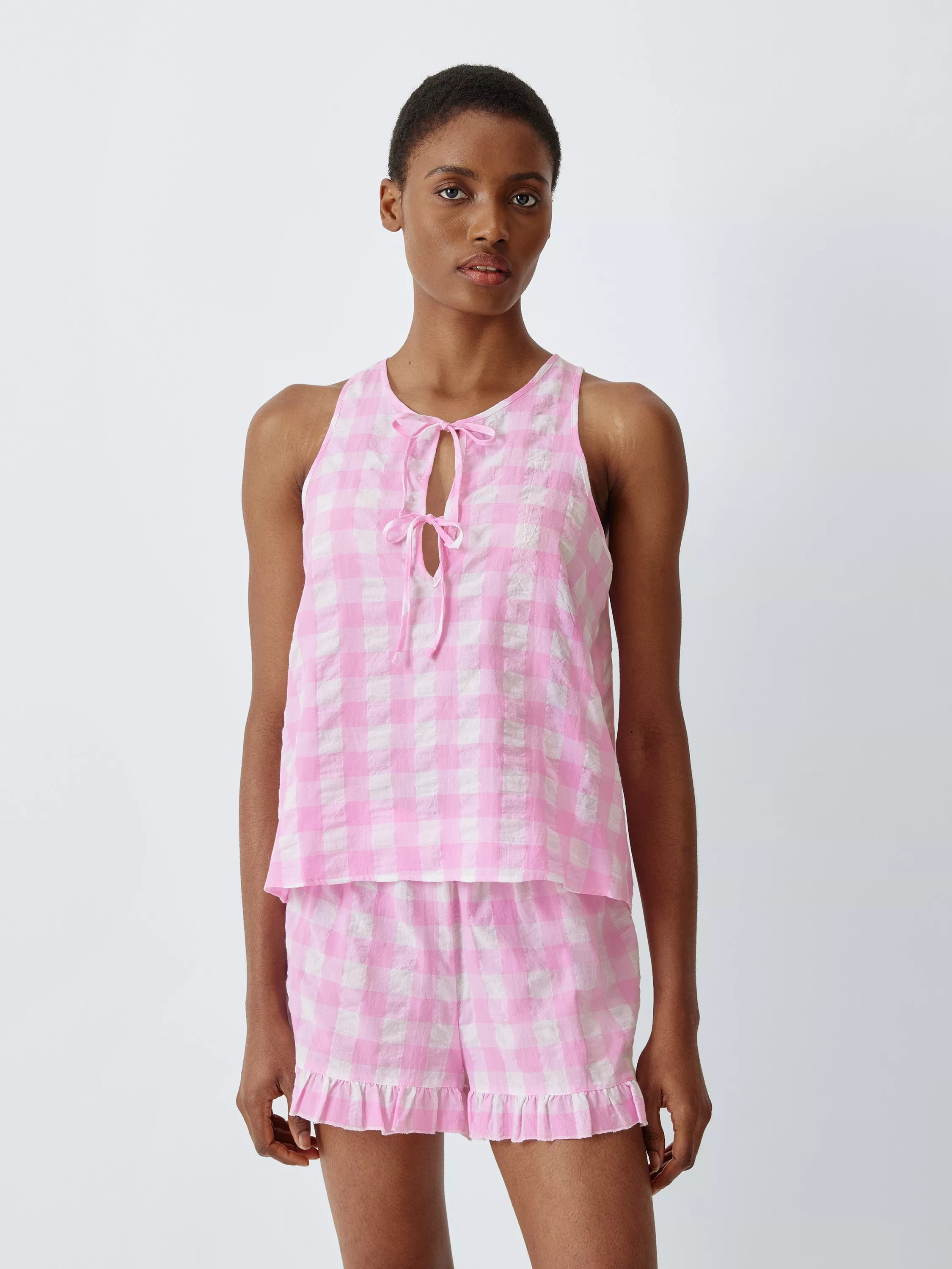 Model wearing pink gingham sleeveless tie-front top and matching ruffle-hem shorts pyjama set on white background