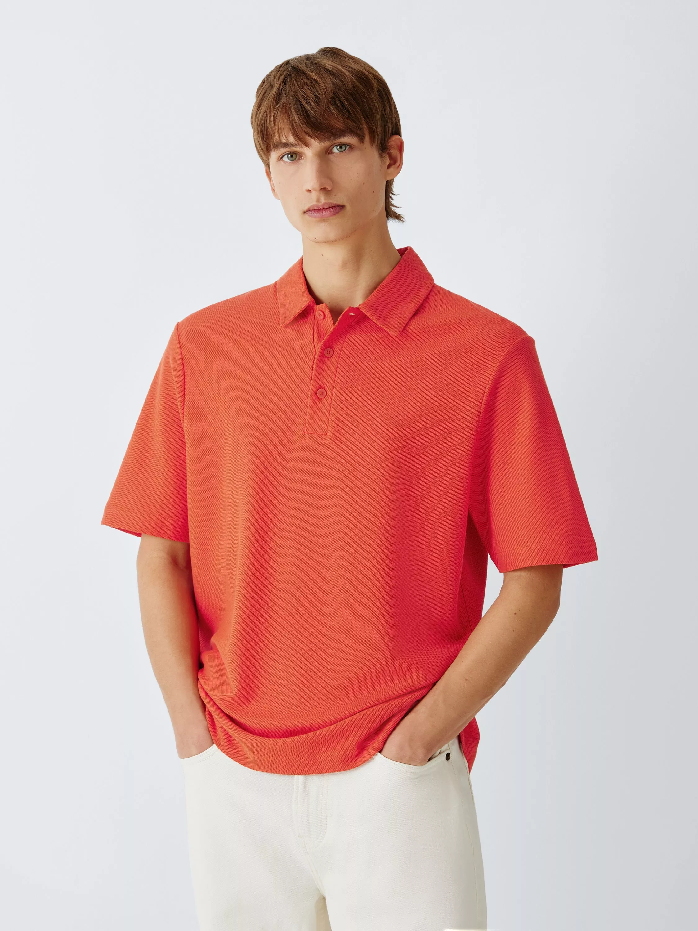 Male model wearing a bright orange short-sleeve polo shirt with collar, styled with white trousers on studio backdrop