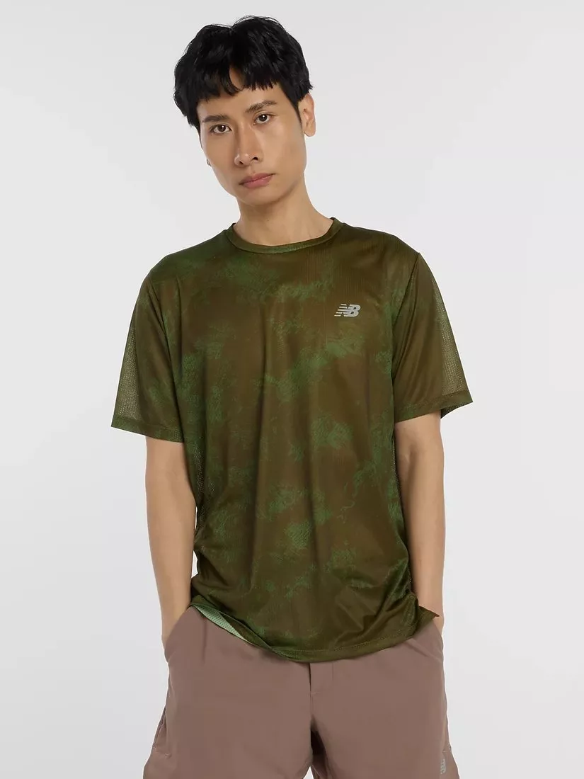A person wearing an olive green New Balance T-shirt and beige shorts stands against a plain background.