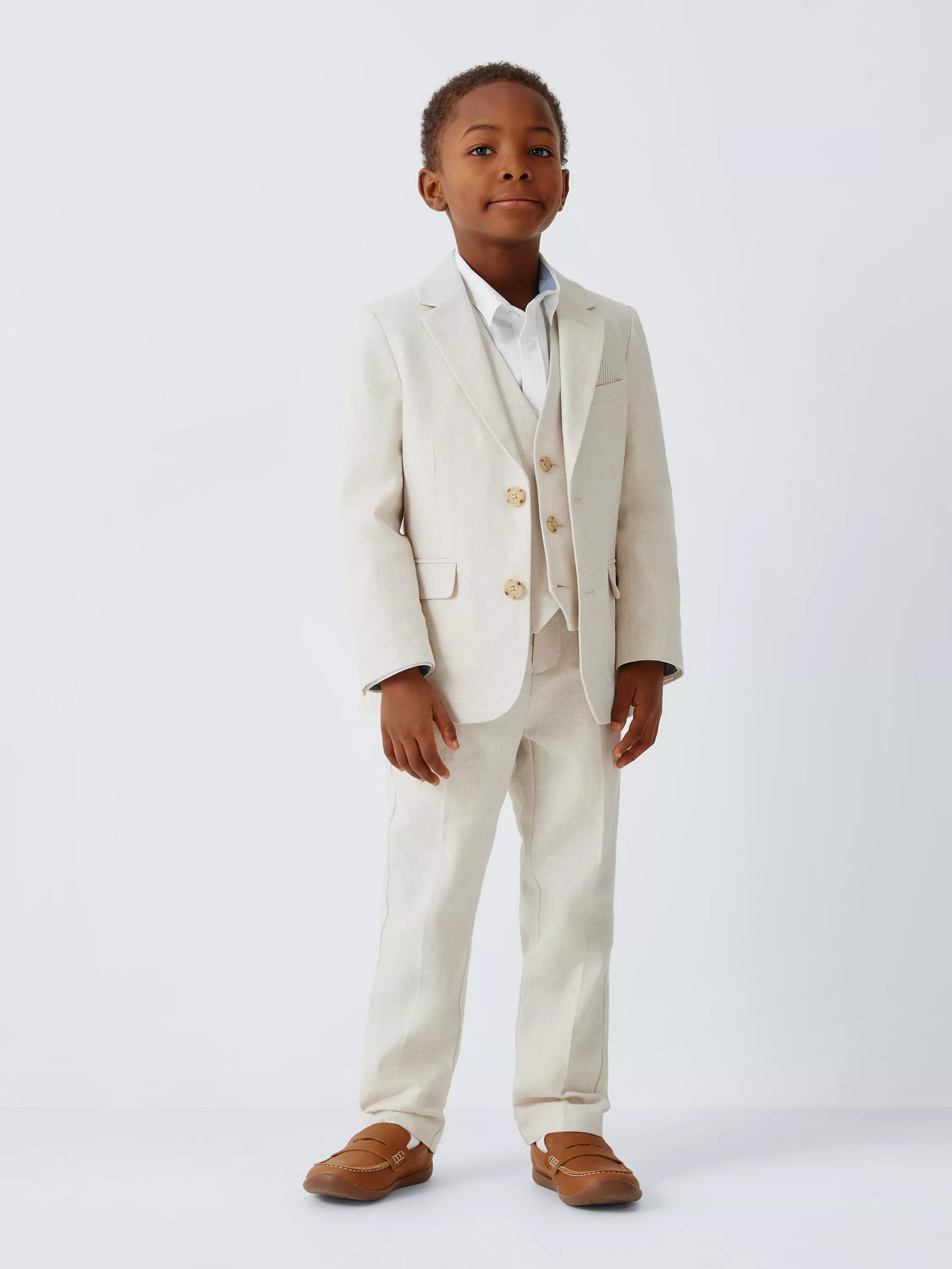Young boy in a beige suit with a white shirt and tan loafers, standing confidently against a plain background.