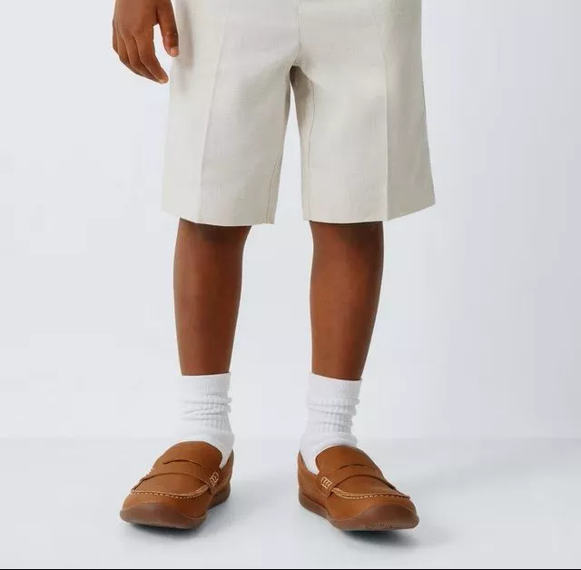 A child wearing beige linen shorts and a white shirt, paired with brown loafers and white socks.