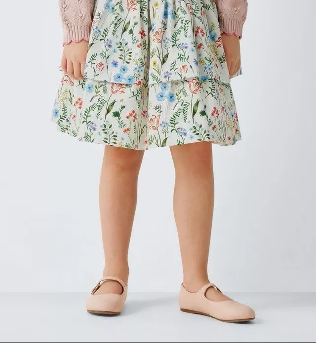 Child in a pink knitted sweater and floral skirt with pastel shoes, standing against a neutral background.