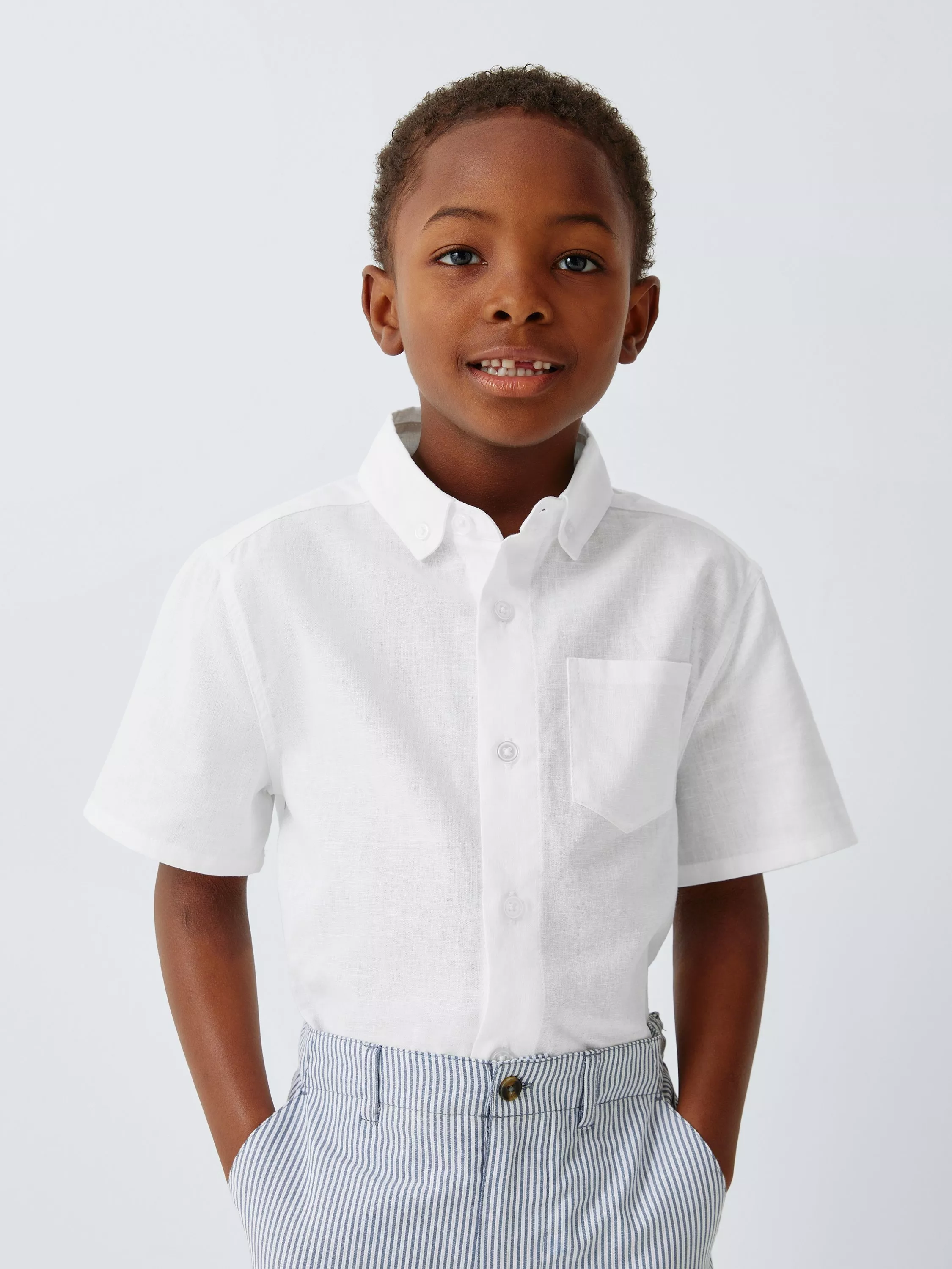 Young boy wearing a white short-sleeve shirt and striped trousers, smiling against a plain background.