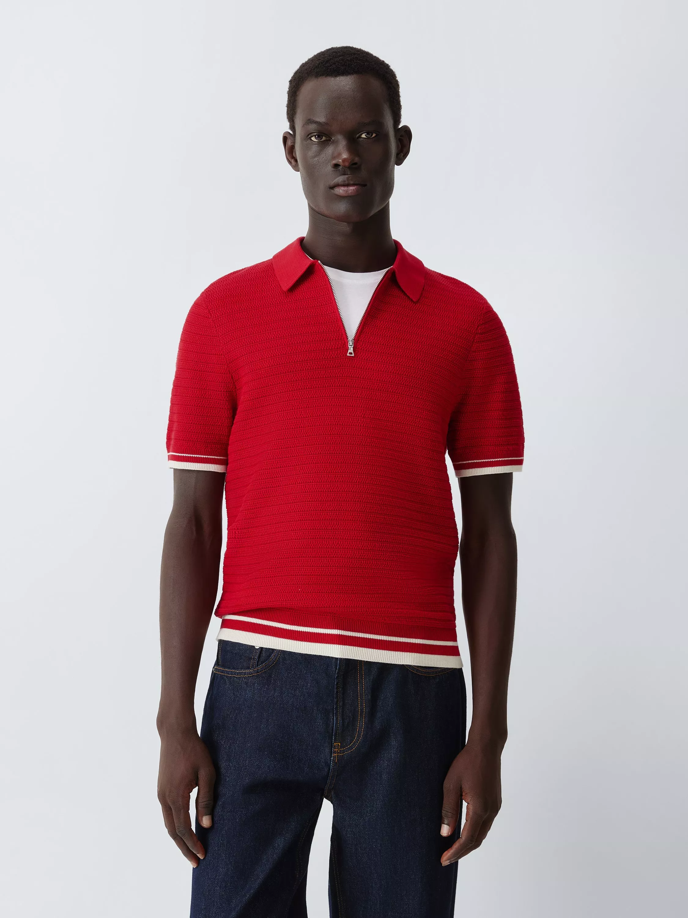 Studio shot of male model wearing red zip-neck polo knit shirt and dark denim jeans on light background