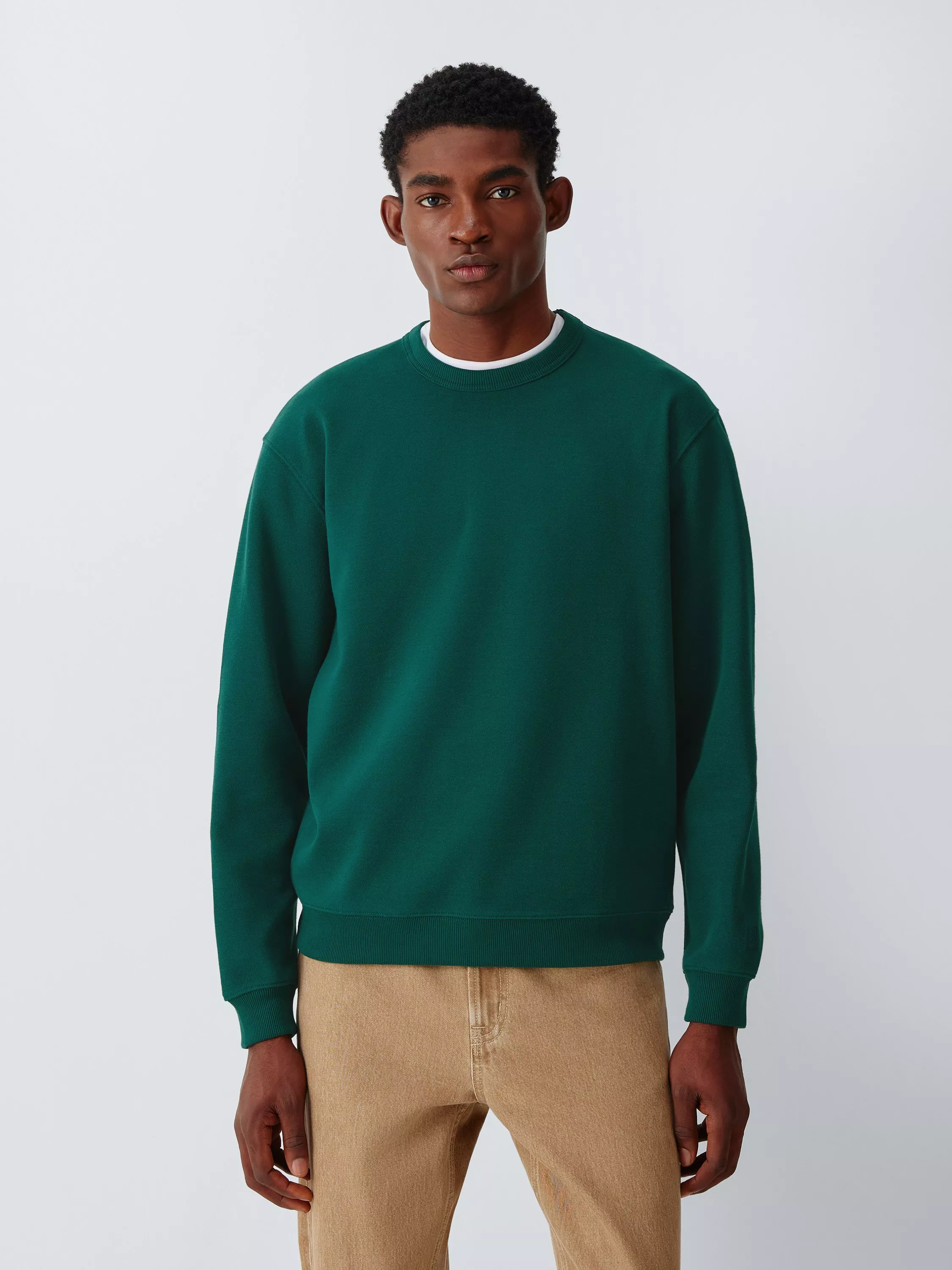 Men’s forest green crew neck sweatshirt with ribbed cuffs, styled with beige trousers in a studio portrait.