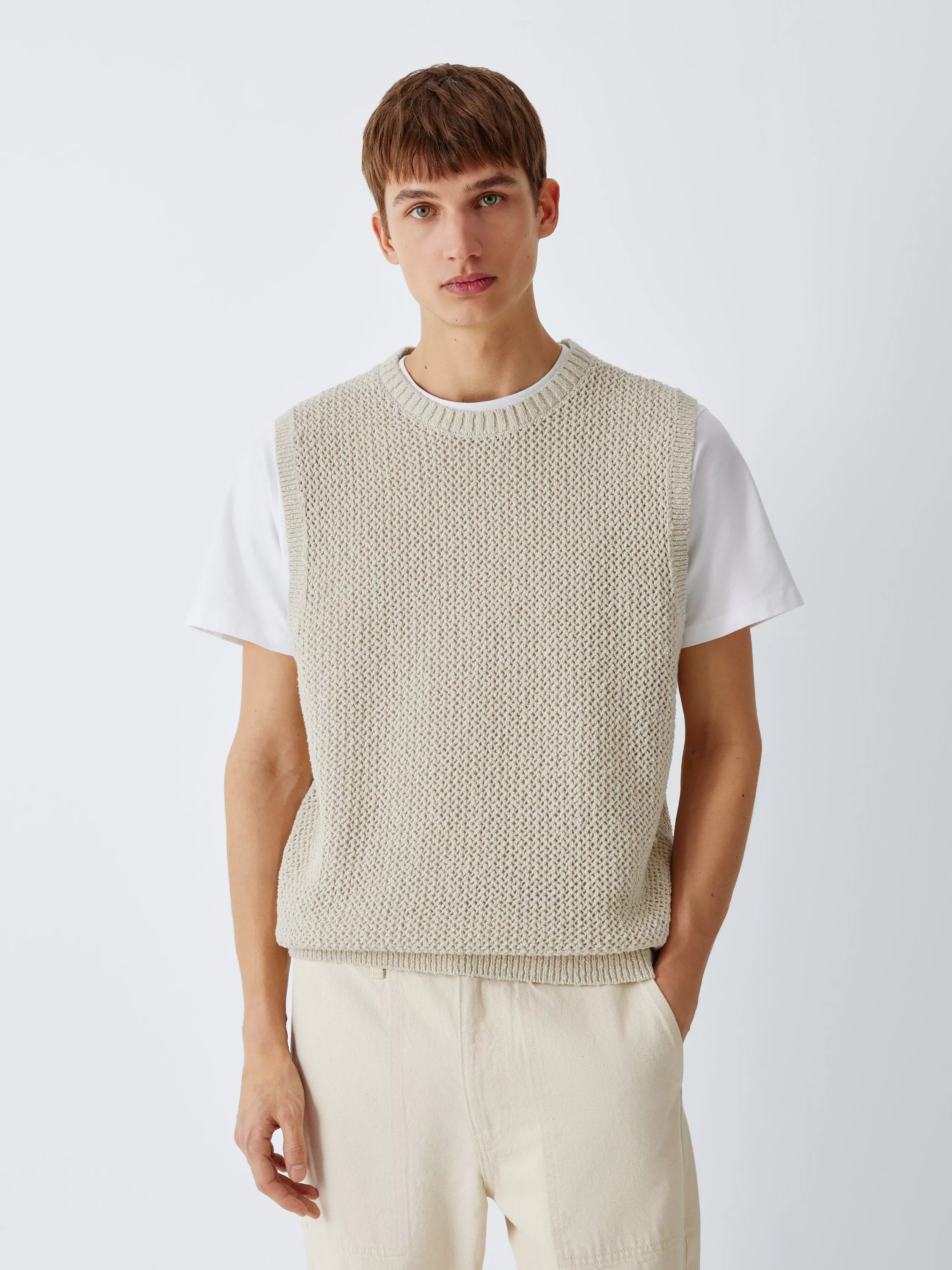 Male model wearing a cream textured knitted tank top over a white T-shirt, studio fashion portrait on grey background