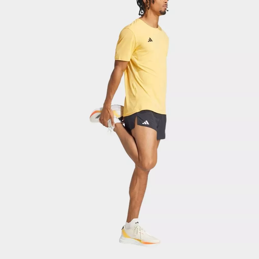Male runner in yellow adidas training T-shirt and black shorts stretching quad, wearing white running shoes