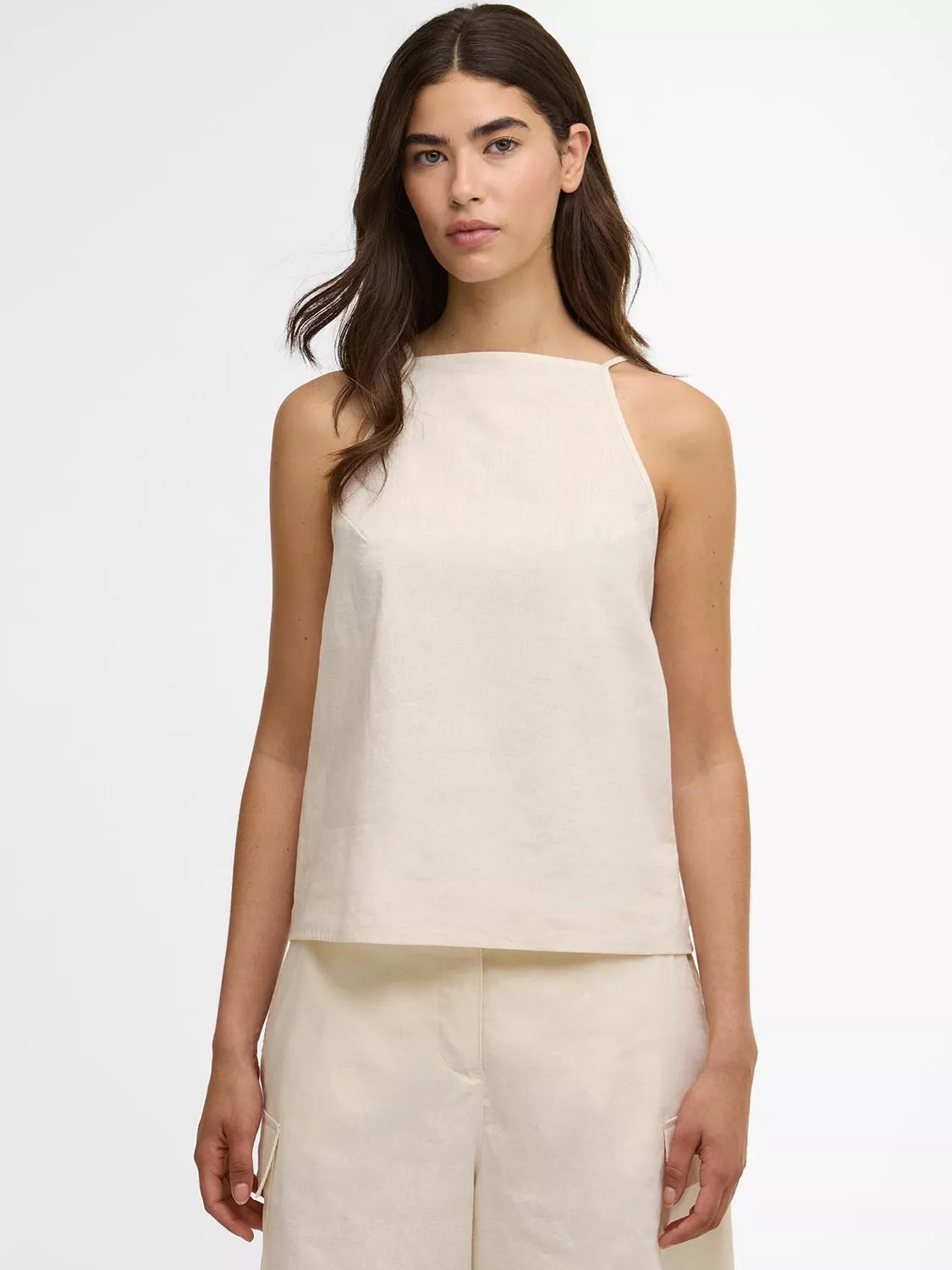 Model wearing cream linen sleeveless top and matching trousers, minimalist summer outfit on white background