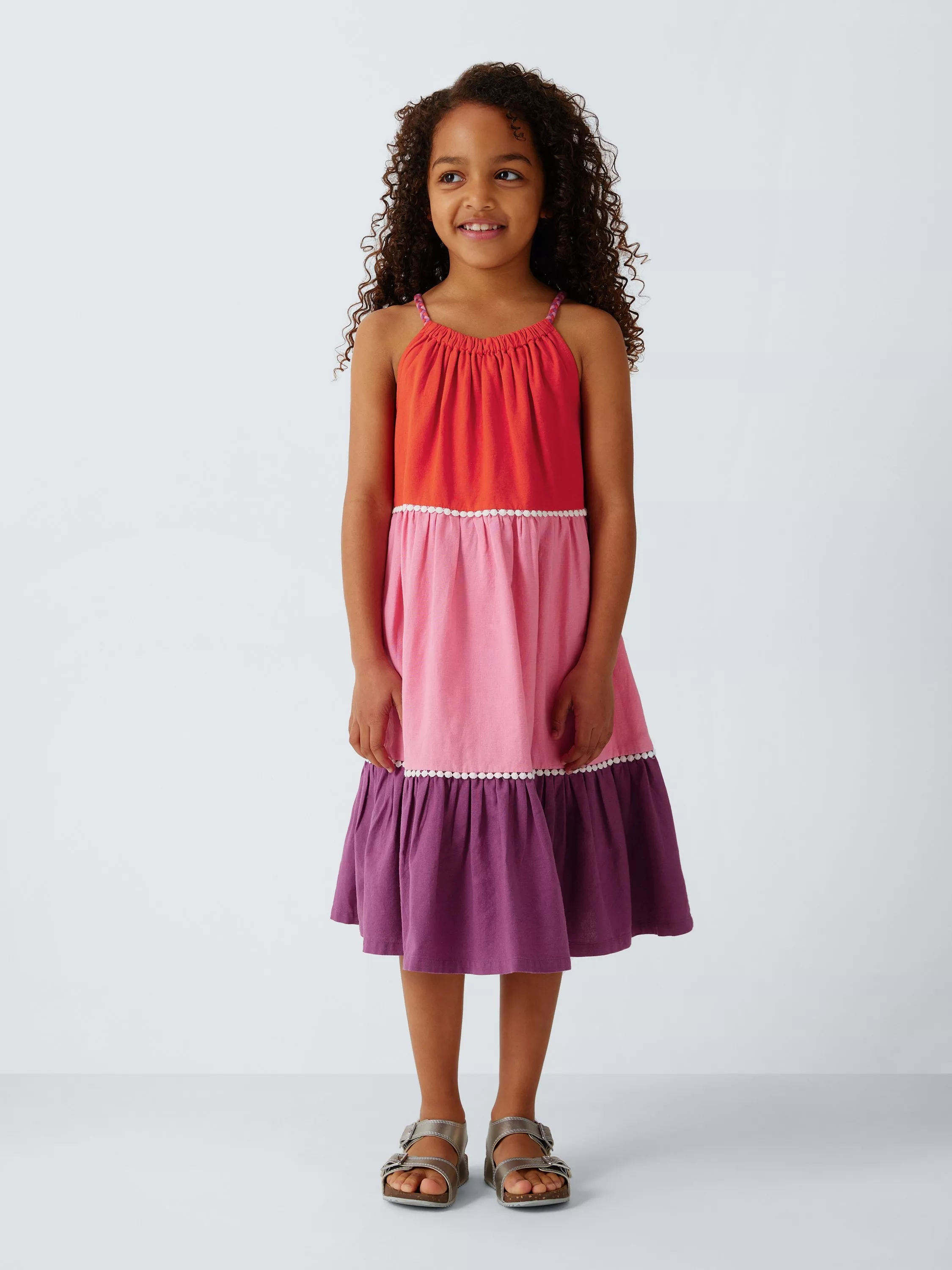 Smiling young girl in a colour-block summer dress in coral, pink and purple, standing in a studio.