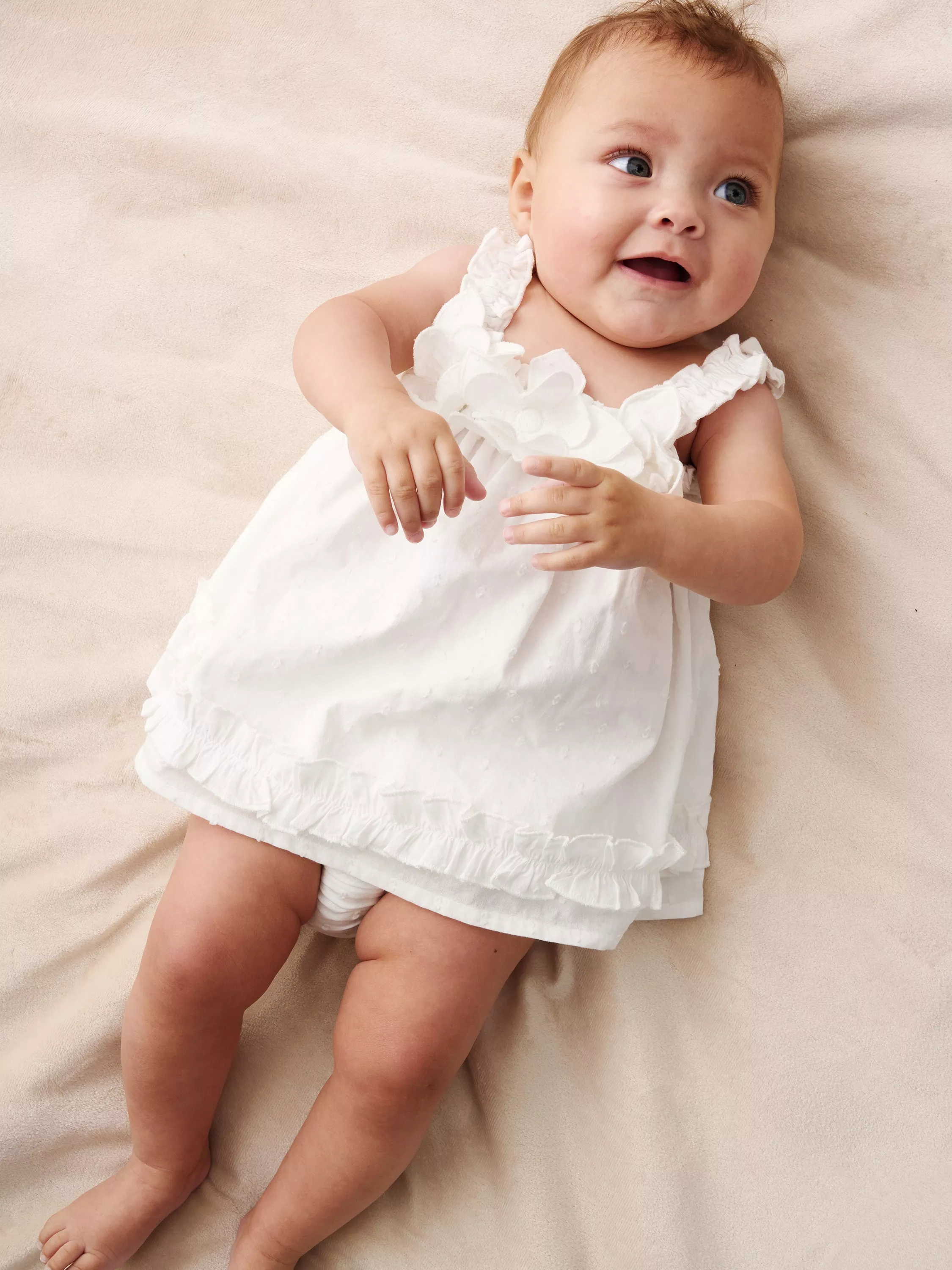 young baby lying down wearing a white summer dress