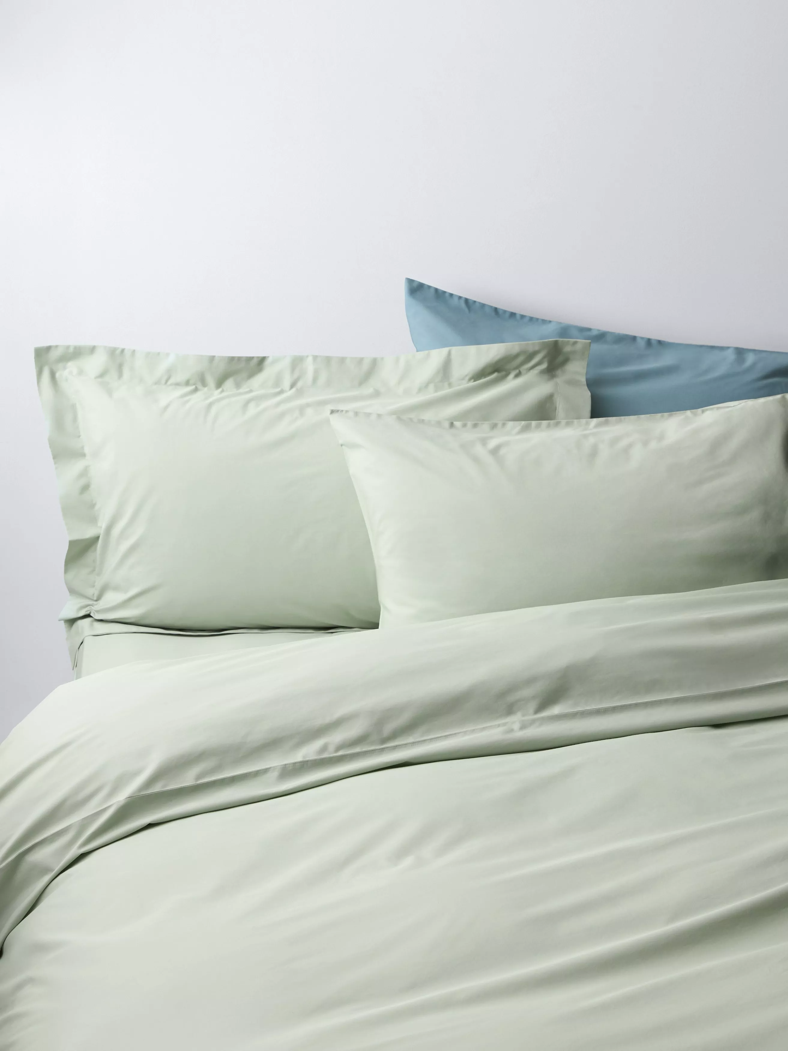 Sage green duvet cover set with matching pillowcases and a blue accent pillow on a neatly made bed