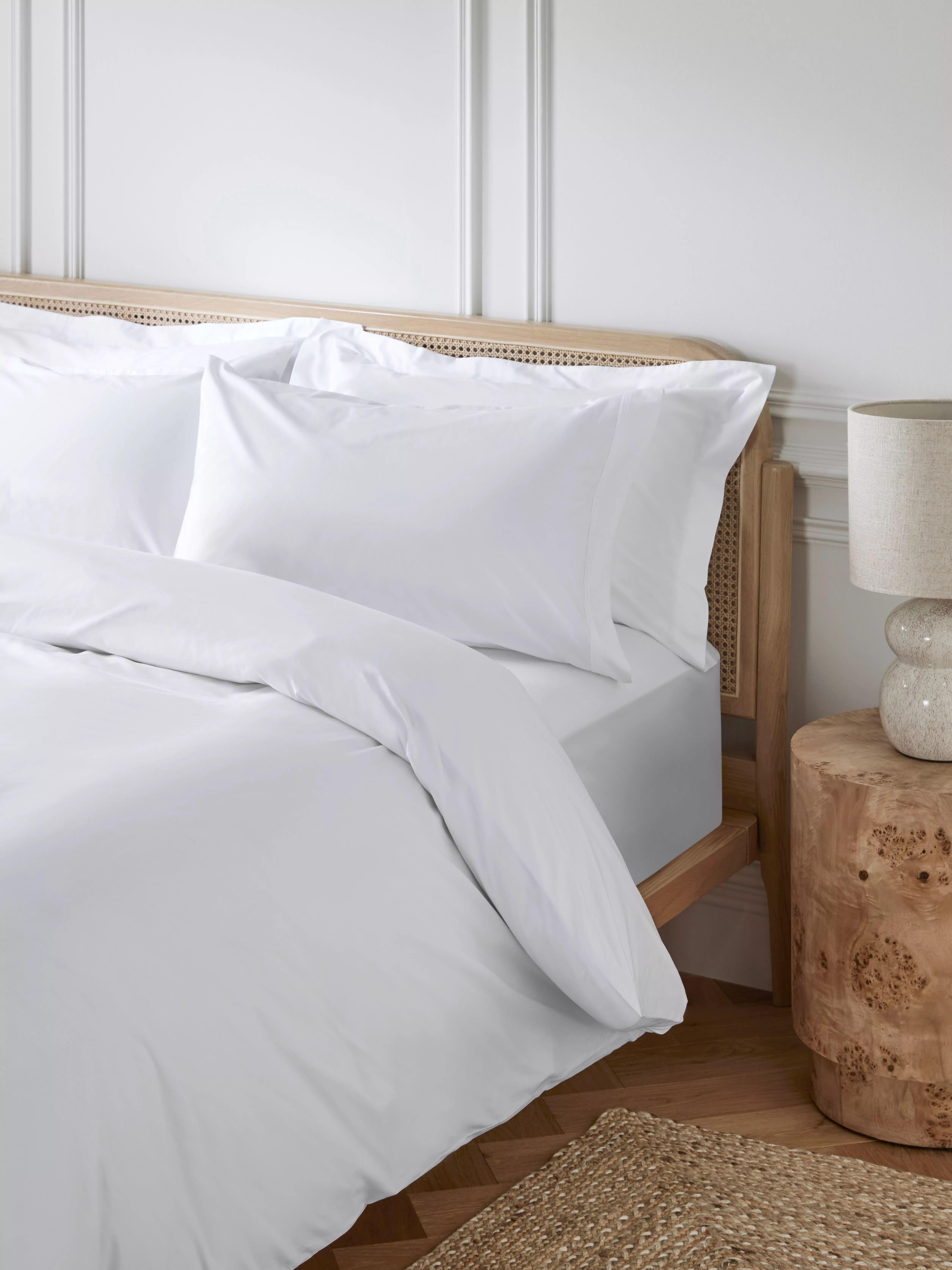 Elegant bedroom with white bedding on a wooden bed, featuring a rustic bedside table and neutral decor.