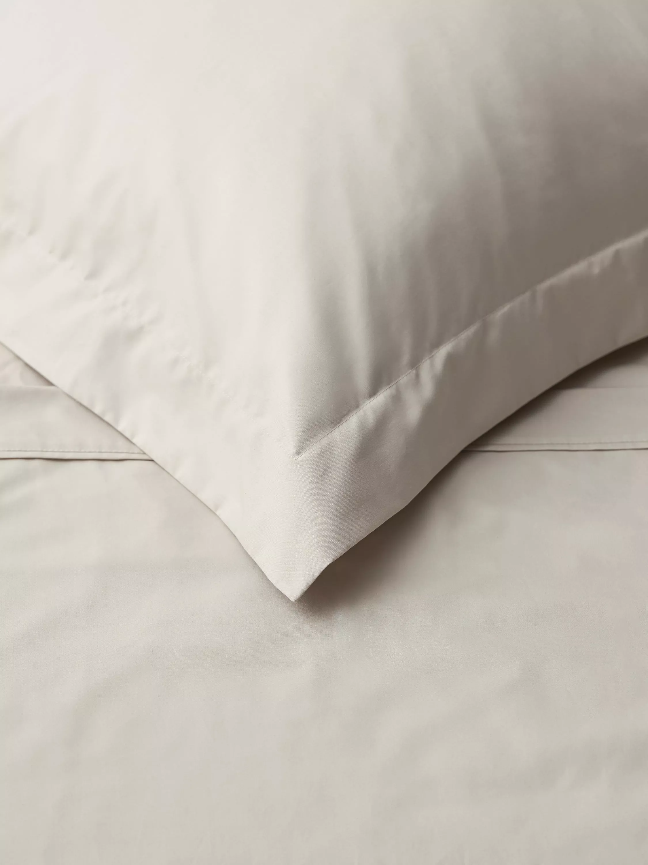 Close-up of white cotton pillowcase and bed sheet with stitched hem, soft hotel-style bedding texture