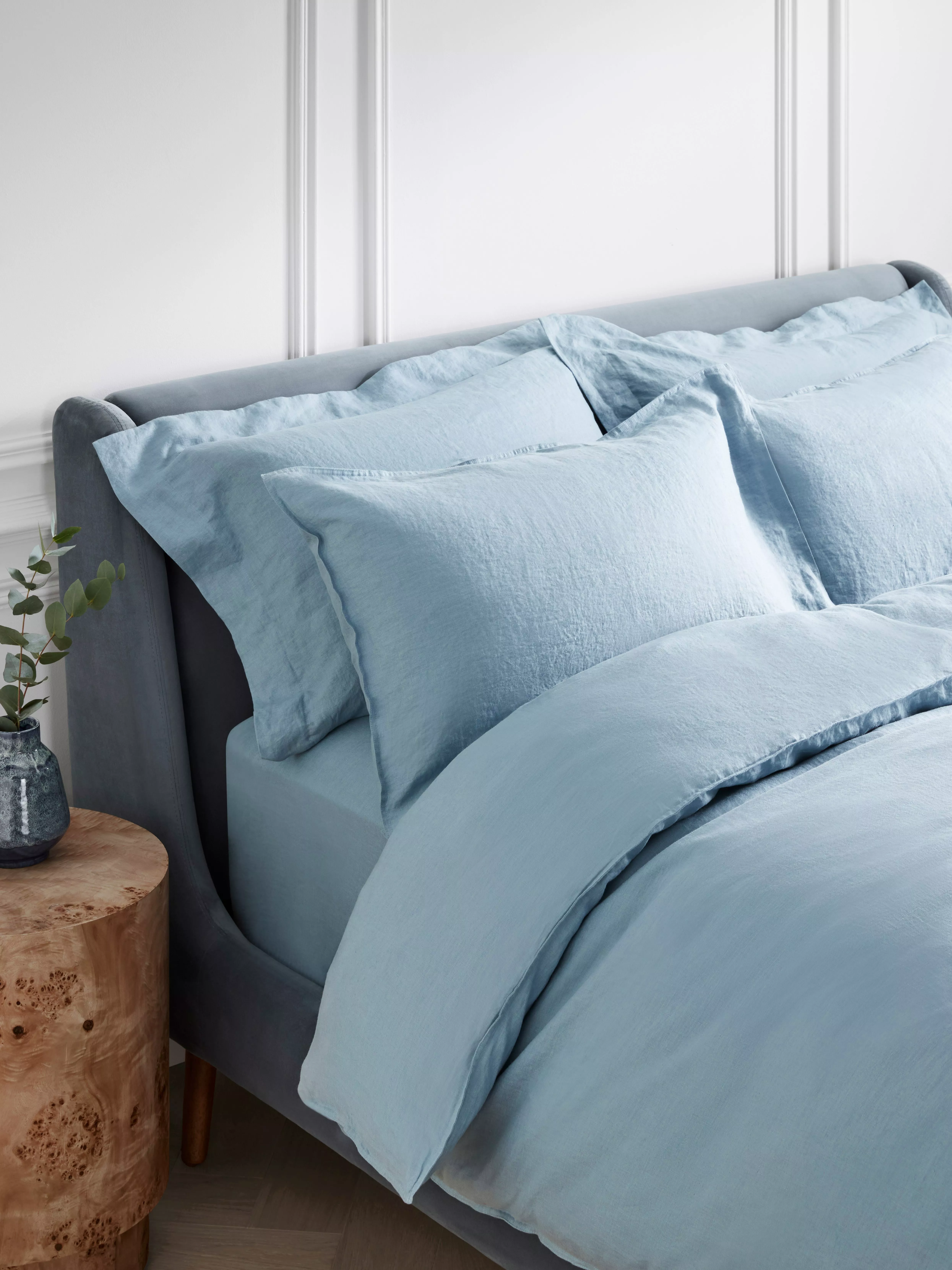 Light blue linen duvet cover and pillowcases on a grey upholstered bed, styled in a modern bedroom setting