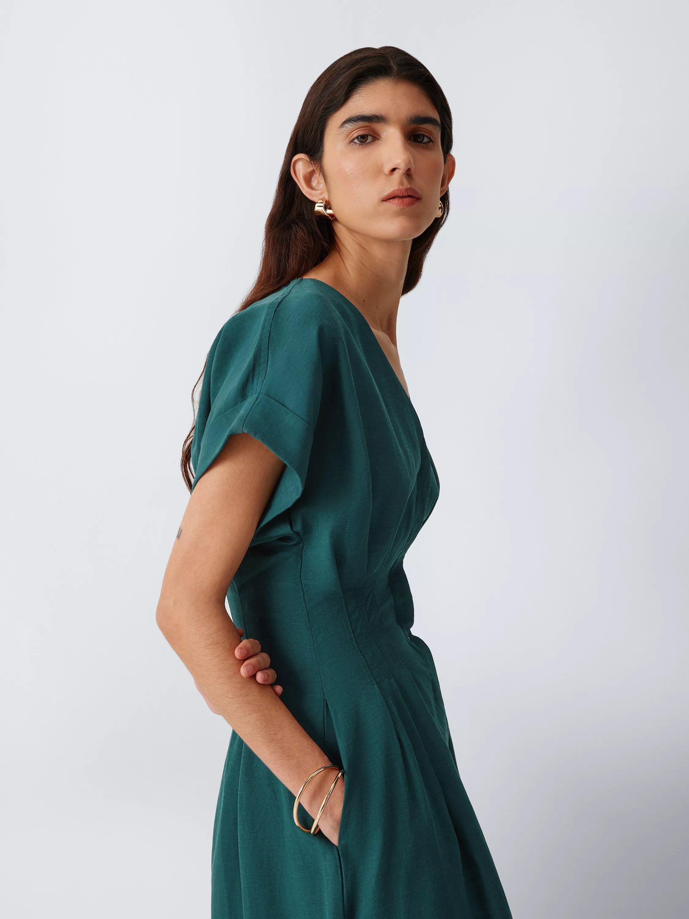 Studio portrait of woman in teal green midi dress with gold hoop earrings and bangles, side pose on grey background