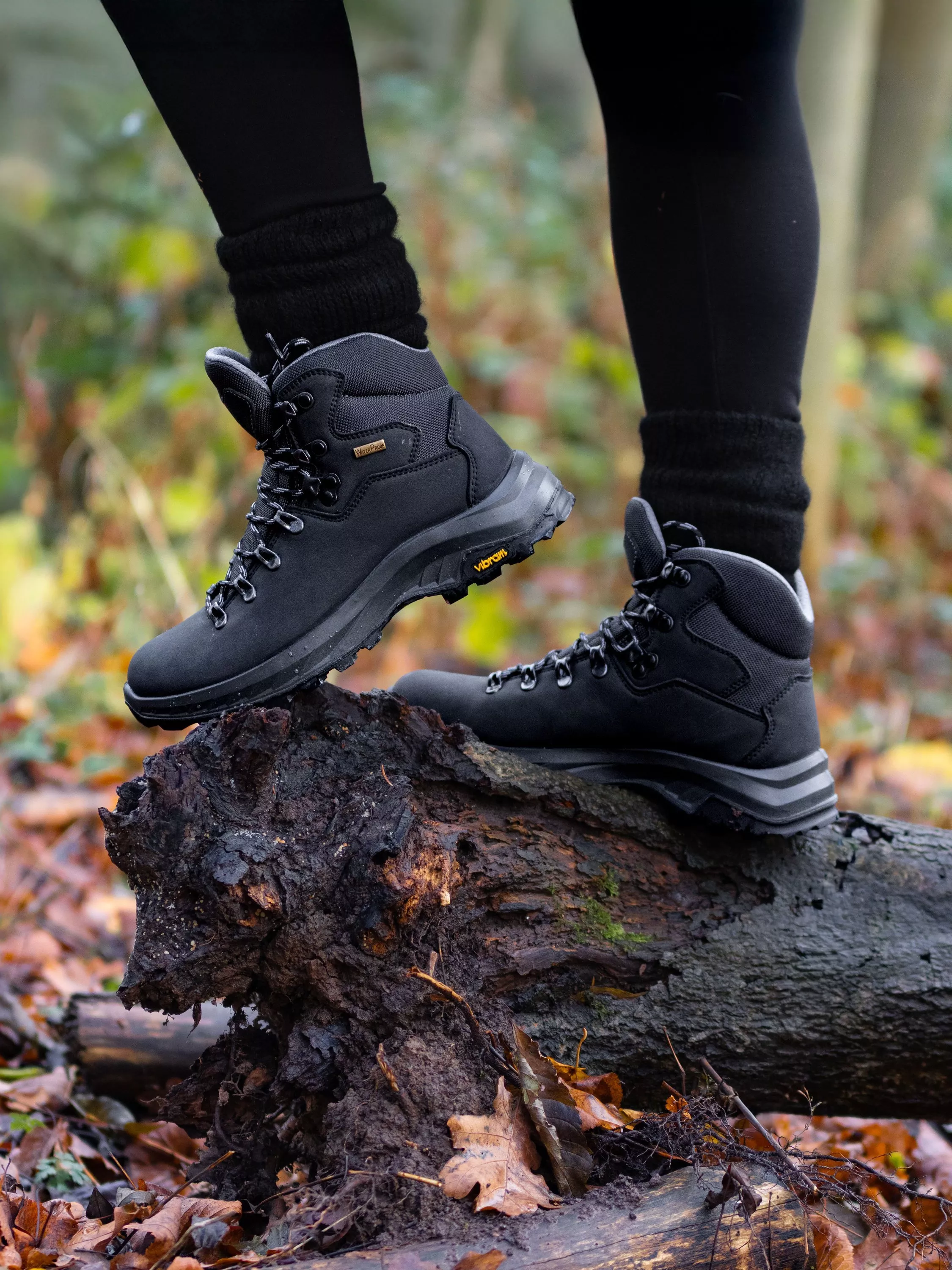 Close-up of black waterproof hiking boots with Vibram soles on a fallen log in autumn woodland.