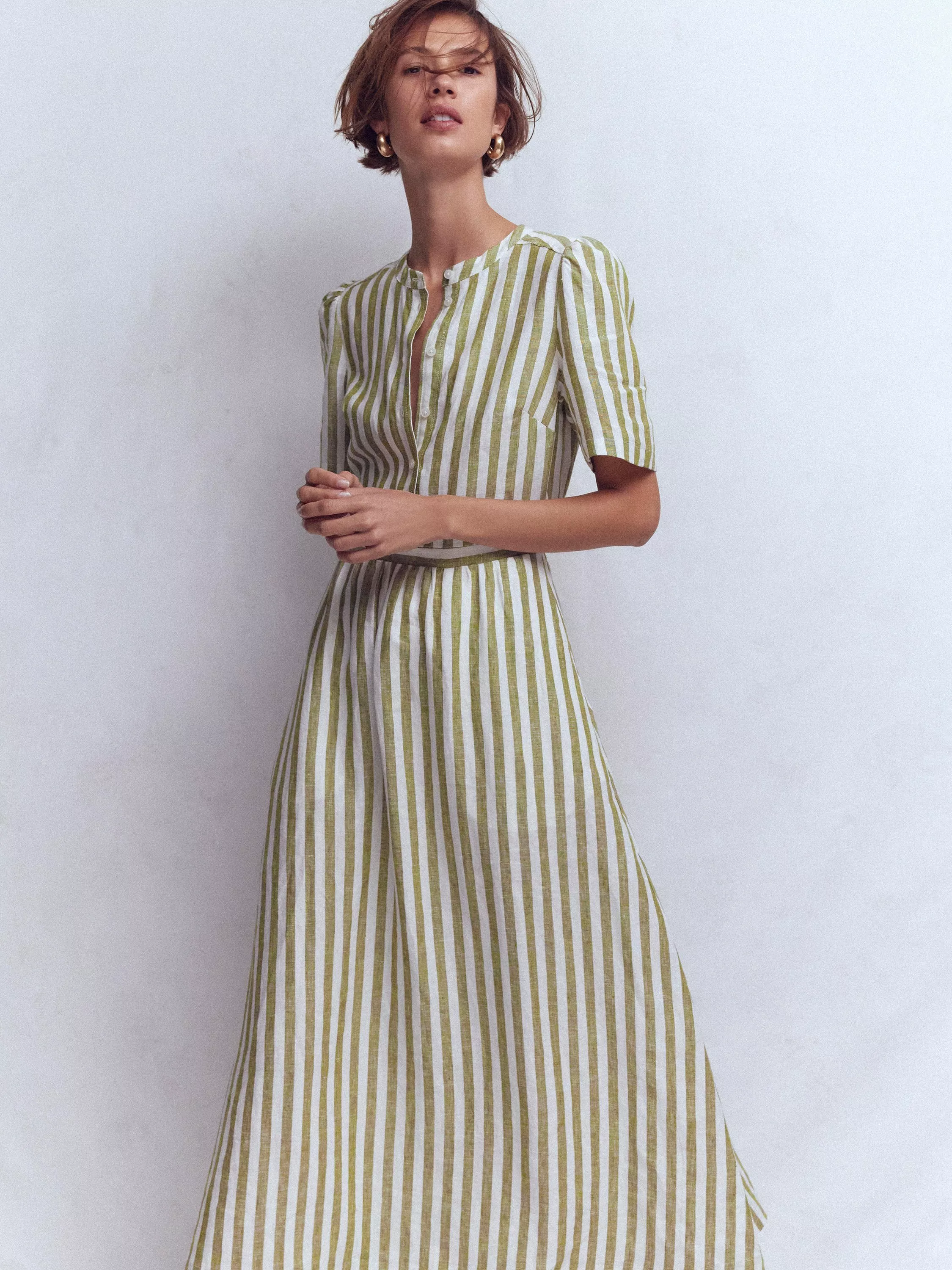 A person wears a green and white striped dress with short sleeves, standing against a plain background.