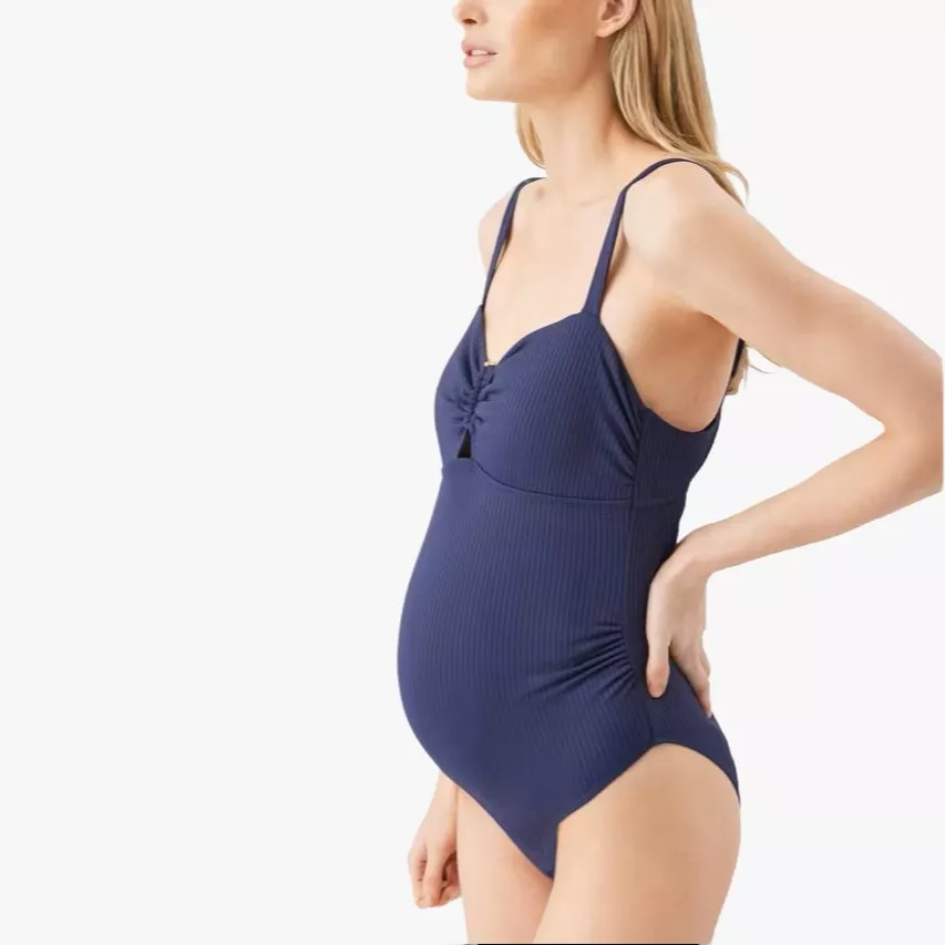 Pregnant model in navy ribbed maternity swimsuit with ruched bust and spaghetti straps, side view on white background