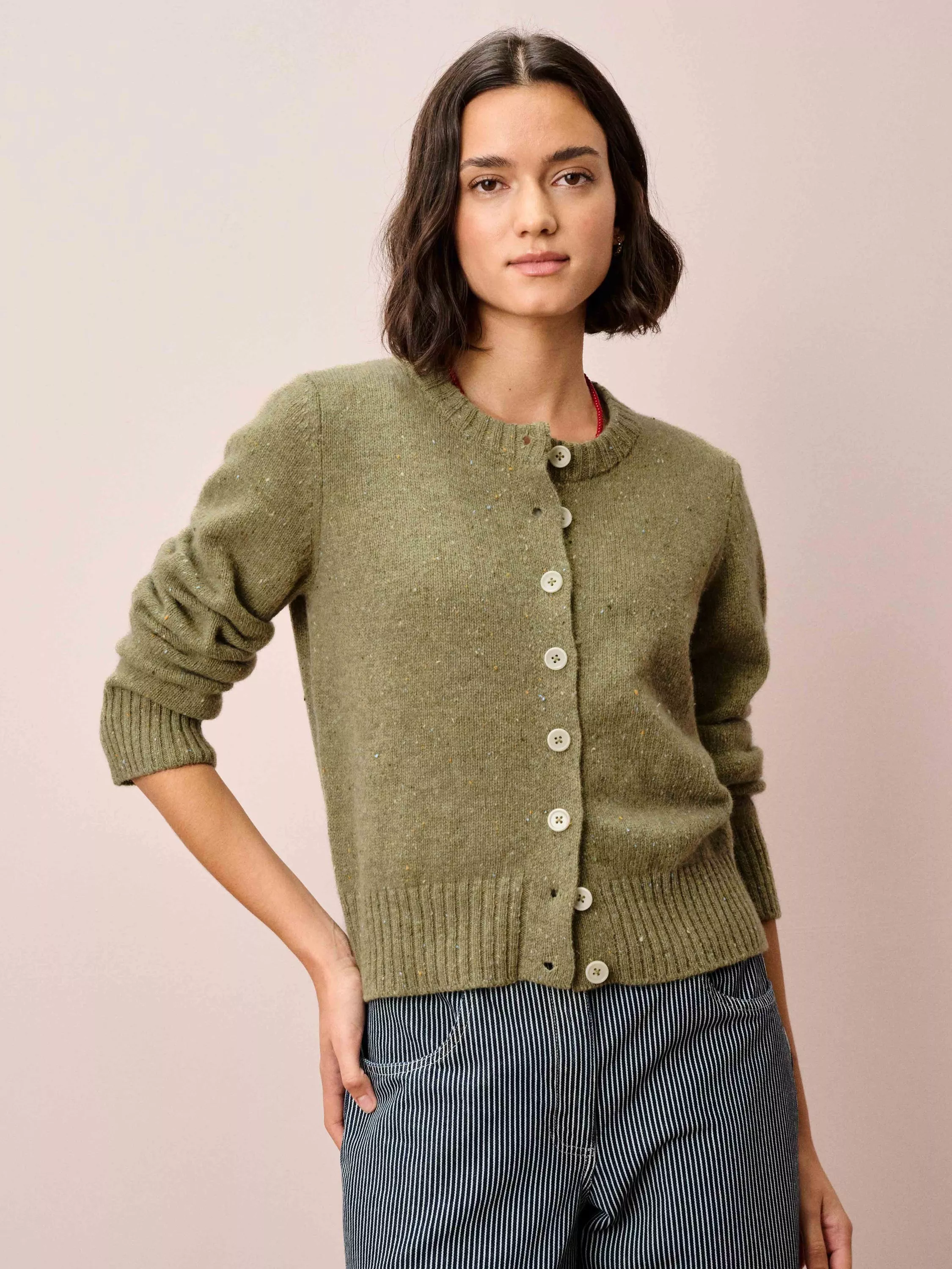 A woman wearing a light green ribbed cardigan with button details, paired with dark blue jeans.