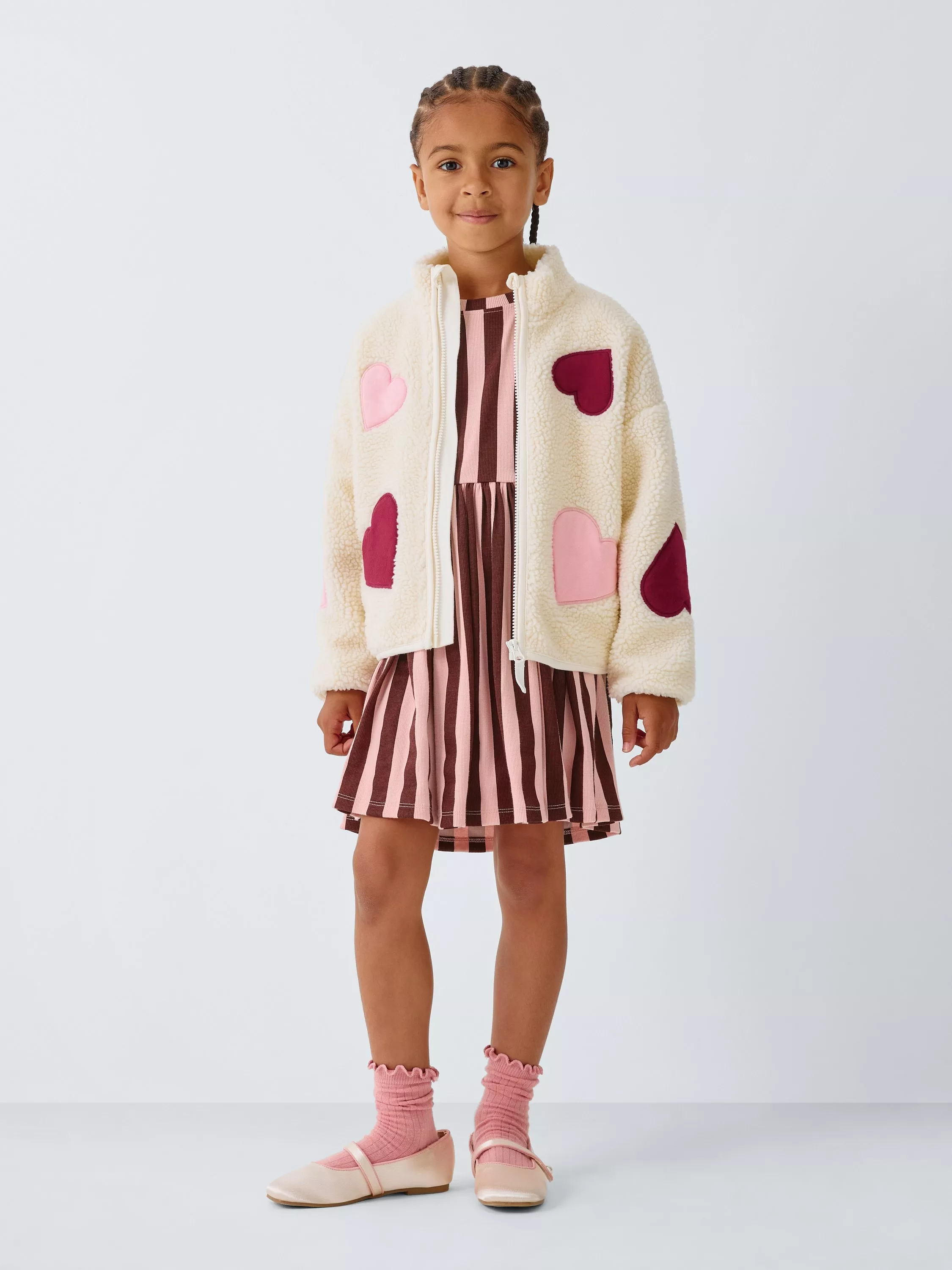 Girl wearing a cream teddy fleece jacket with heart patches and a pink striped dress, studio fashion photo